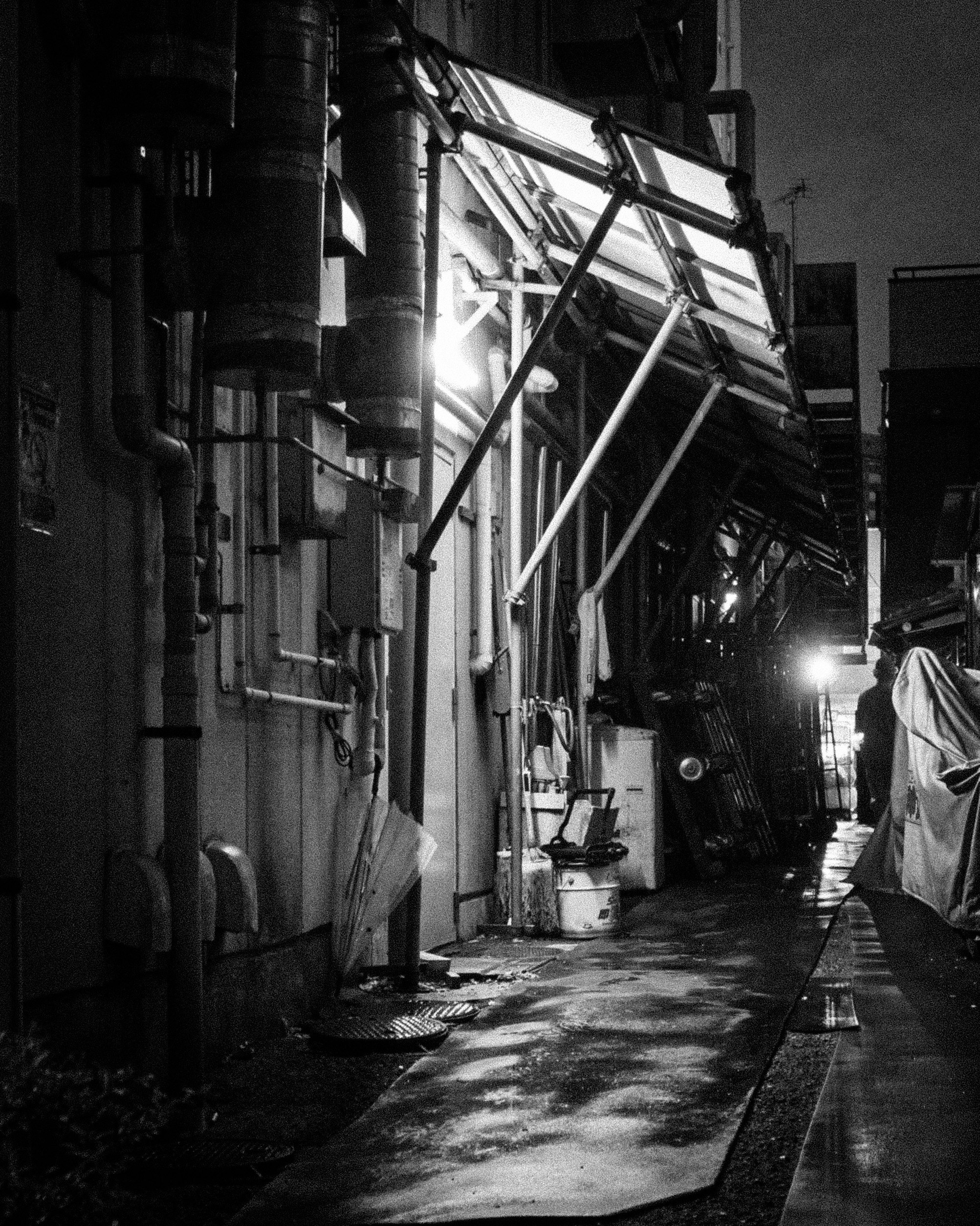 路地裏の工業設備と配管が並ぶ夜の通路