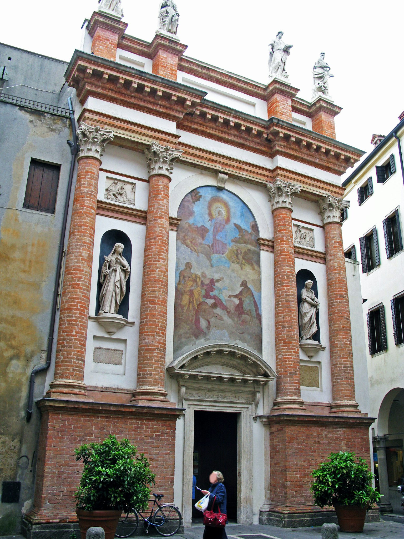 Femme se tenant devant la façade en brique d'une église avec deux statues et une belle fresque