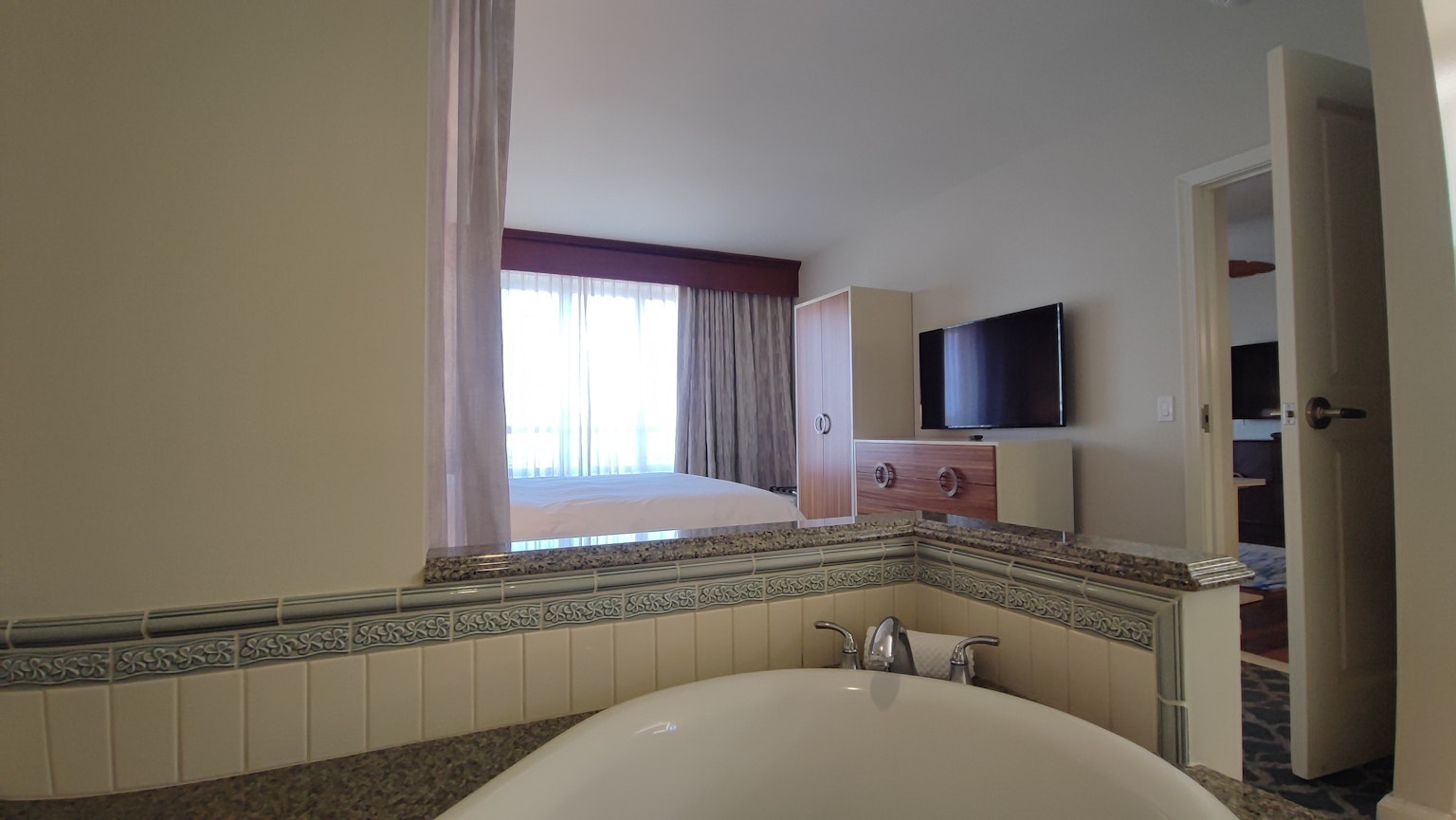 Vue d'une chambre d'hôtel lumineuse depuis la salle de bain avec baignoire et télévision
