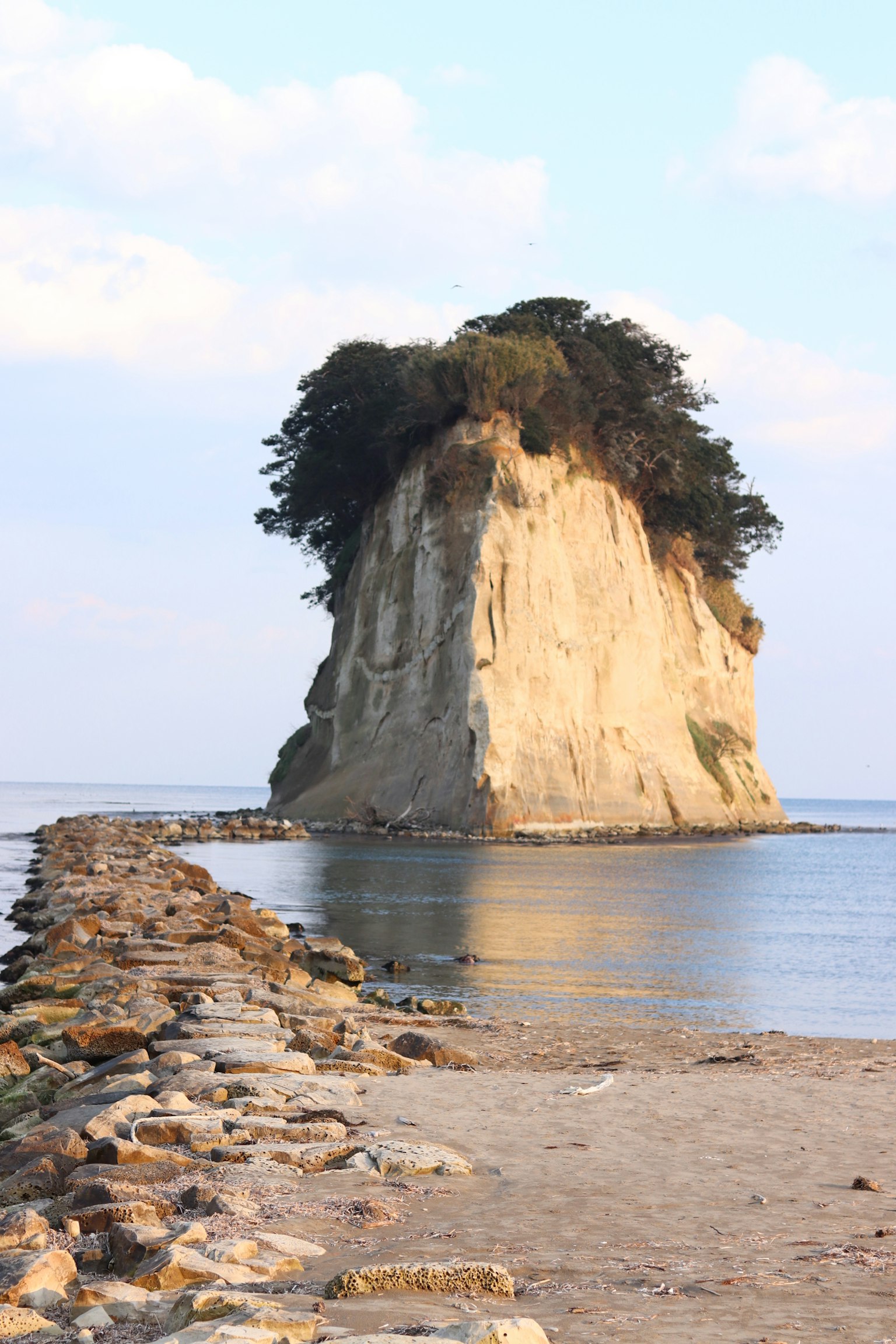 Une île rocheuse avec des arbres entourée d'eau calme et d'un jetée en pierre