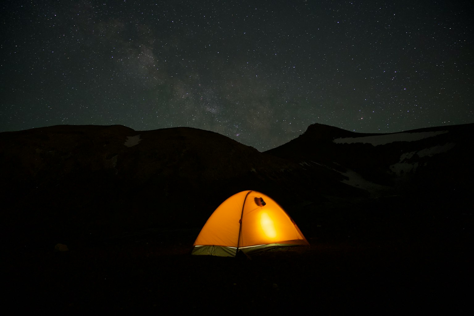 Tienda amarilla brillante bajo un cielo estrellado con siluetas de montañas