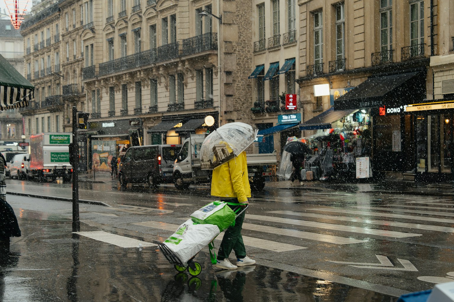 Una persona con un impermeabile giallo che cammina con un ombrello in una strada piovosa di Parigi