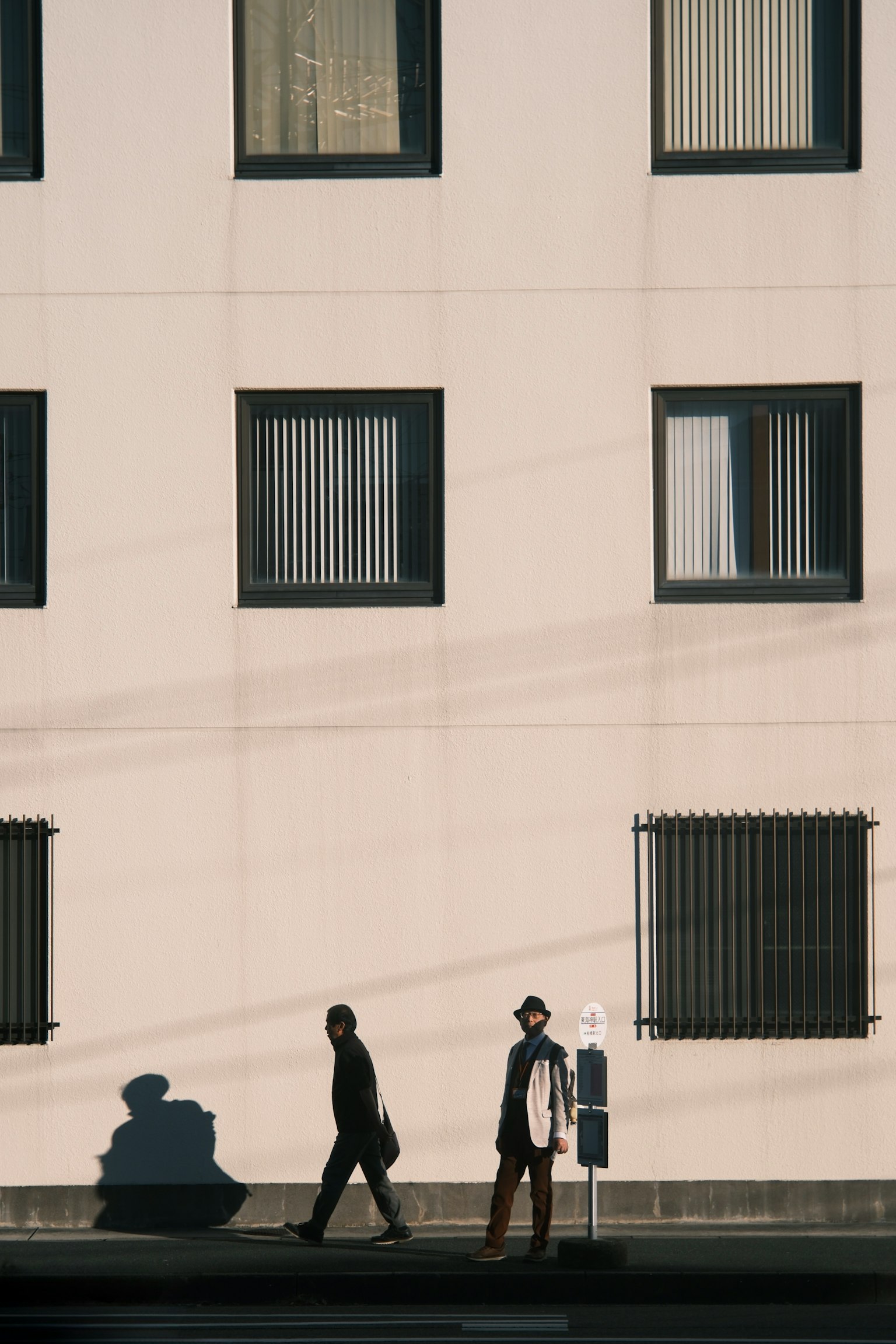 人々が歩いている壁の前のシーン 窓と影が特徴的な建物