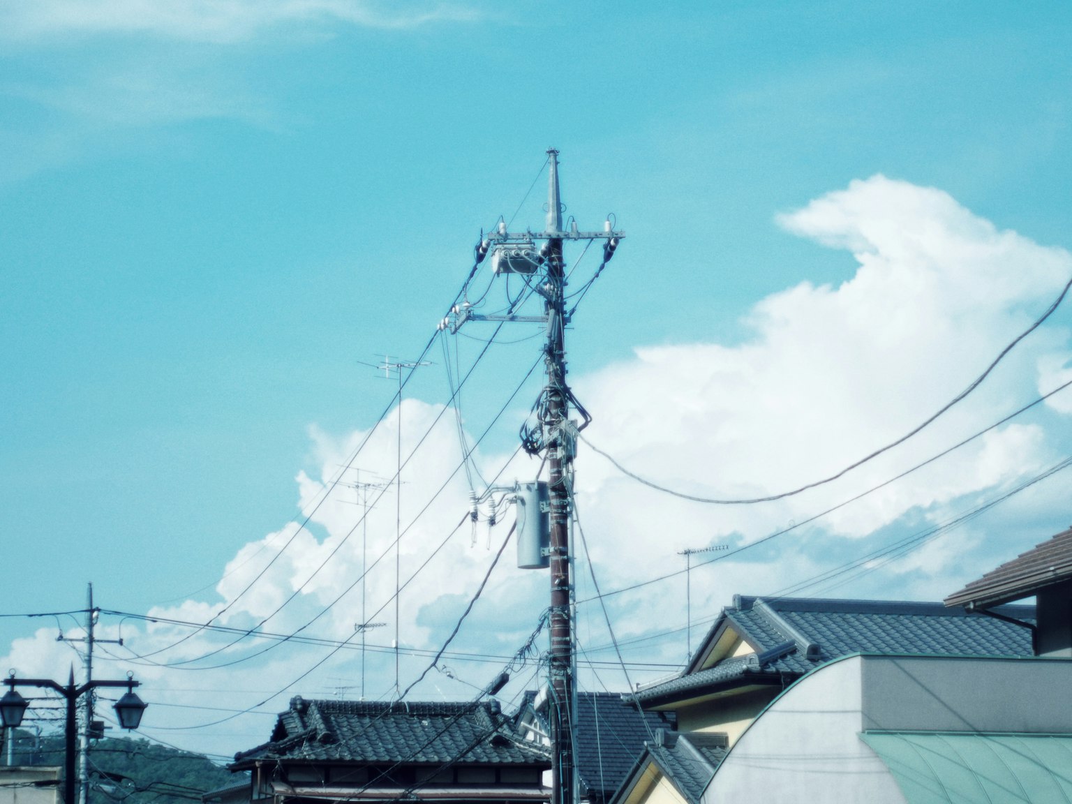 View of utility poles and wires against a blue sky with white clouds