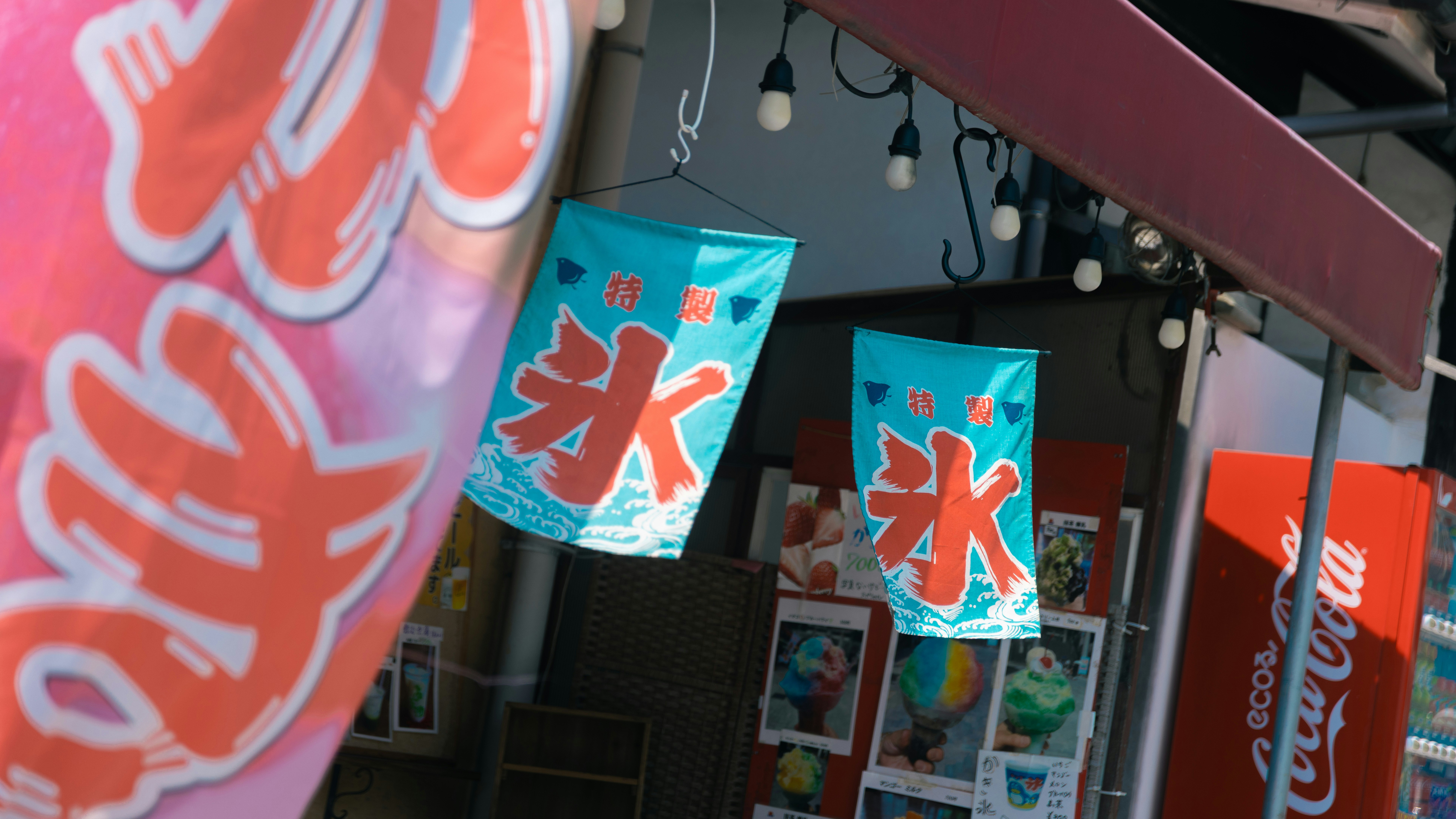 店先に並ぶ赤い暖簾と「氷」デザインの旗のある屋台風の通り