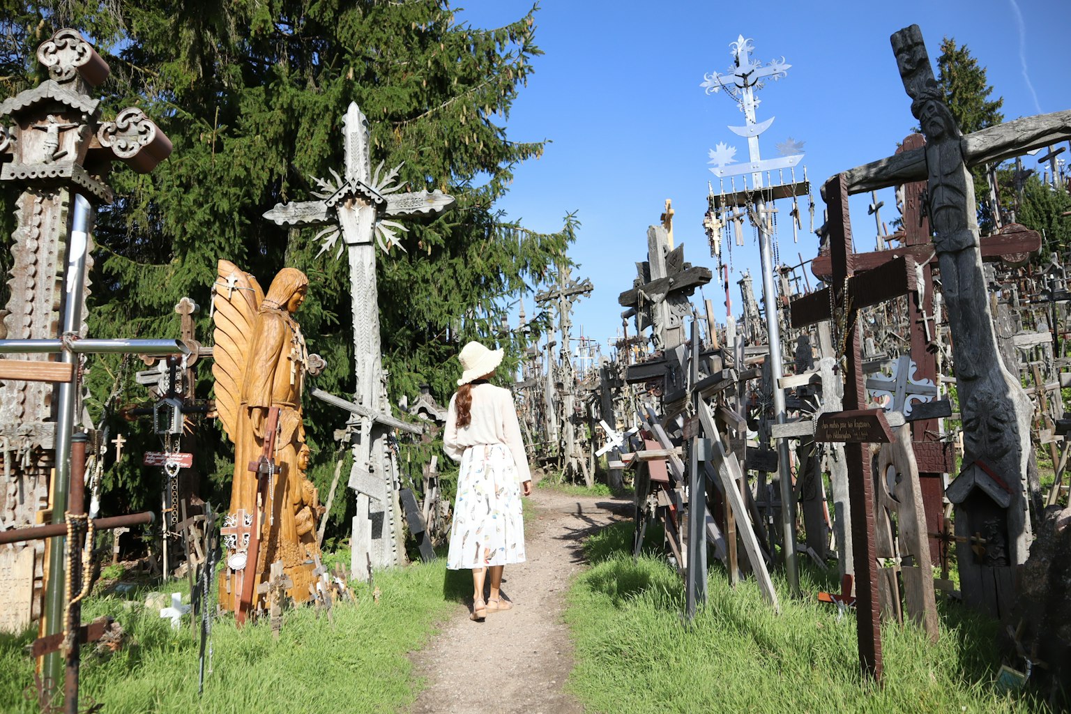 Una donna in abito bianco che cammina tra croci di legno in un cimitero verdeggiante