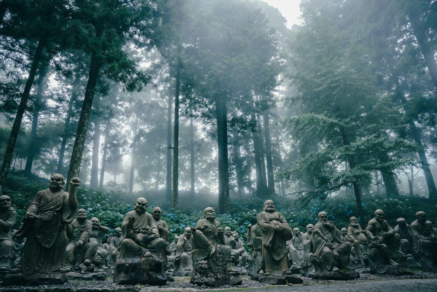 Un groupe de statues en pierre dans la brume avec de grands arbres en arrière-plan
