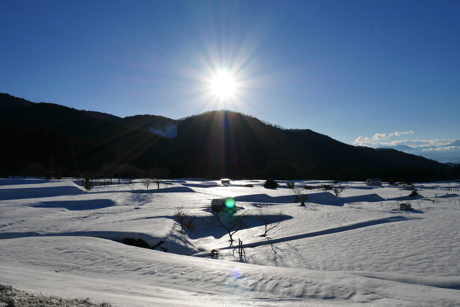 Paisaje nevado con siluetas de montañas y un sol brillante