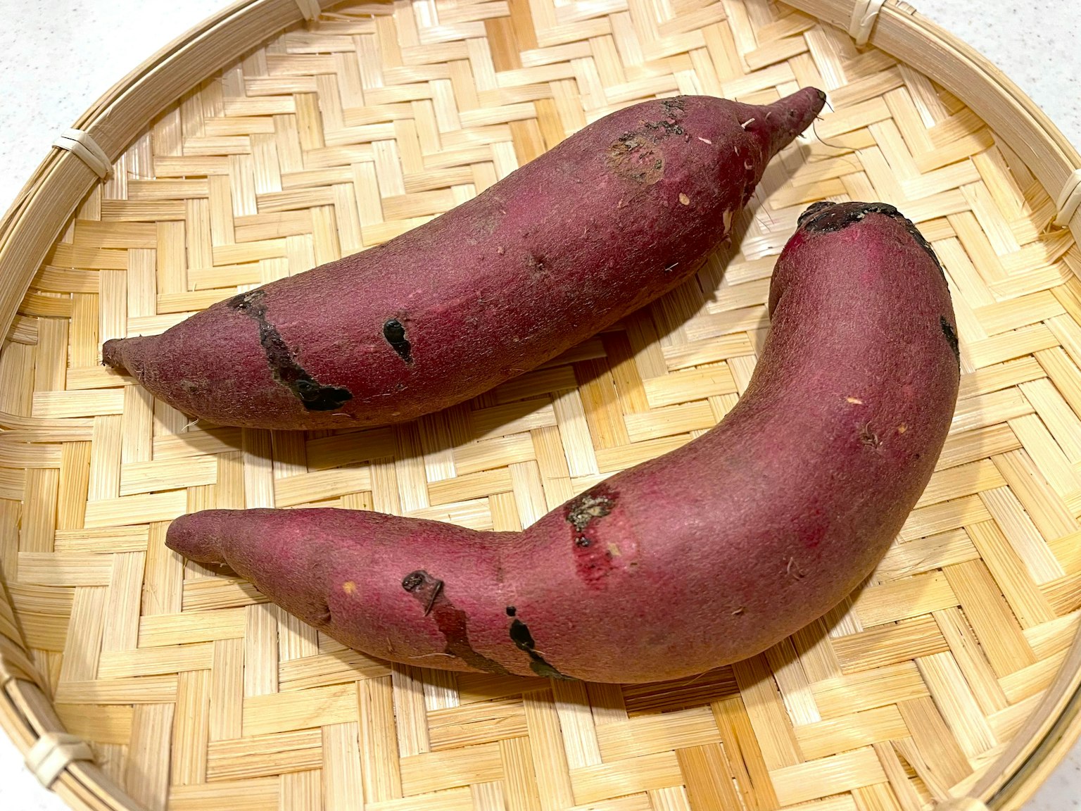 Zwei lila Süßkartoffeln in einem geflochtenen Bambuskorb platziert