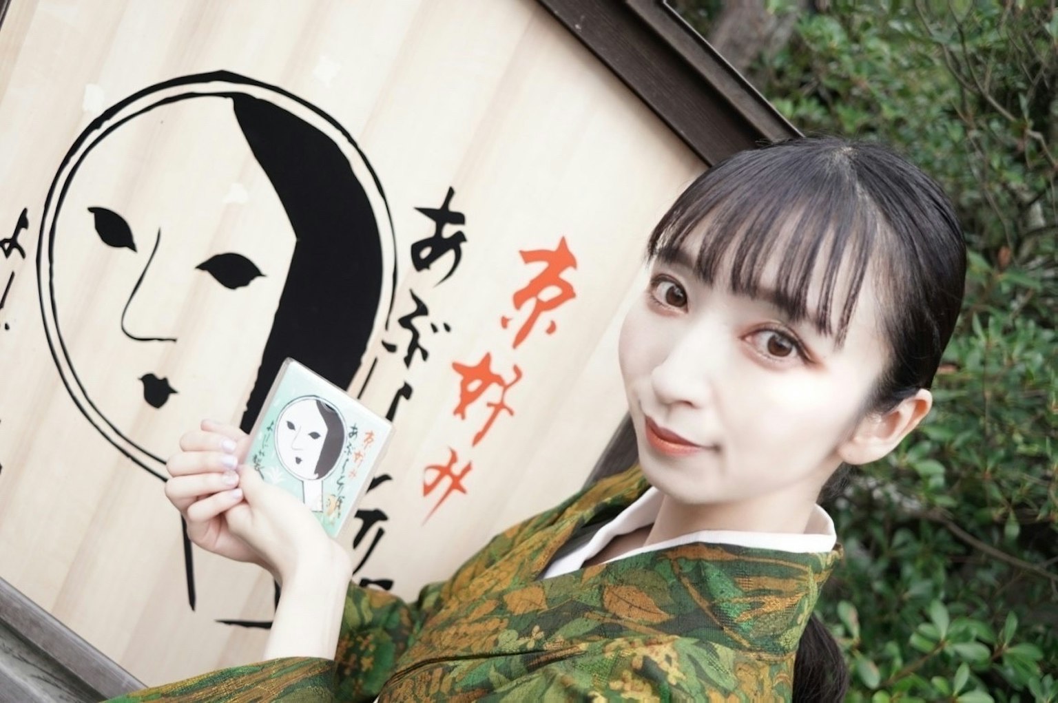 一位穿着和服的女性与墙上的面孔画作合影
