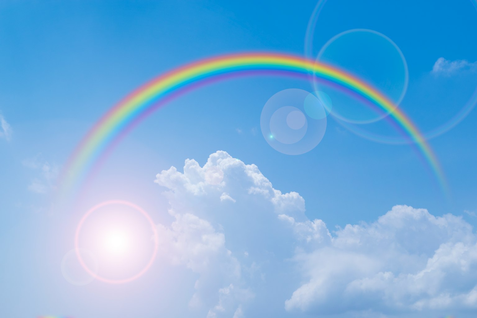 Un arcobaleno che attraversa un cielo blu con nuvole soffici e luce solare