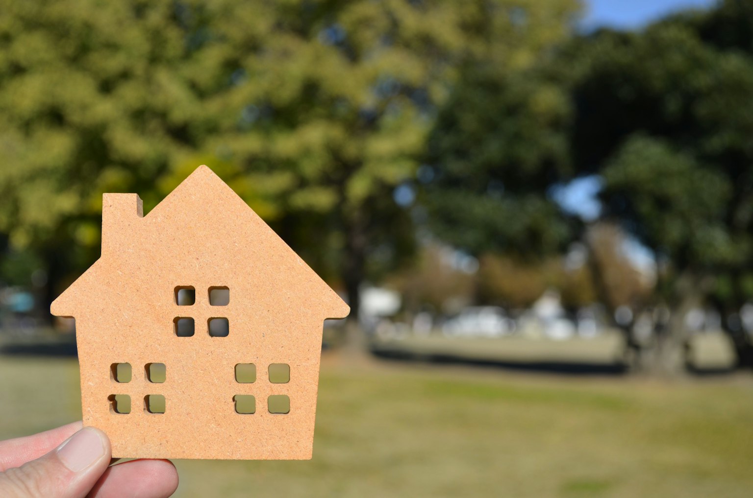 Une main tenant une forme de maison découpée devant un arrière-plan d'arbres verts