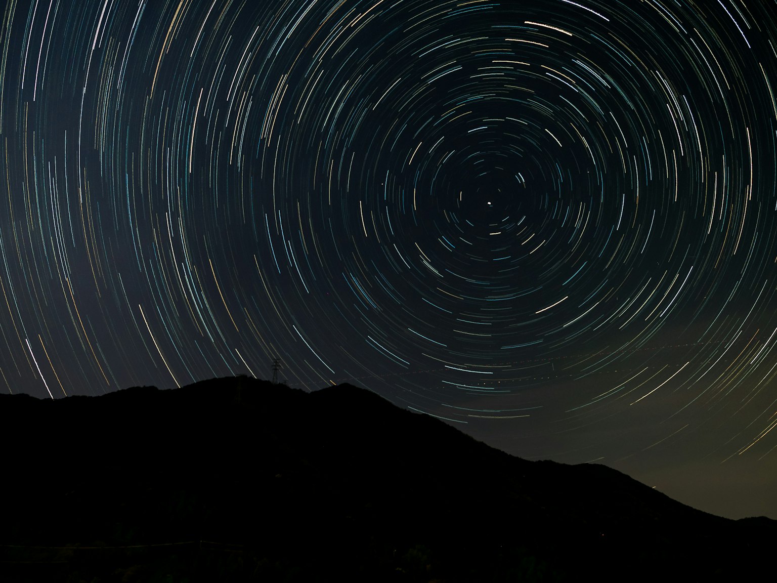 Night sky with star trails and silhouette of mountains