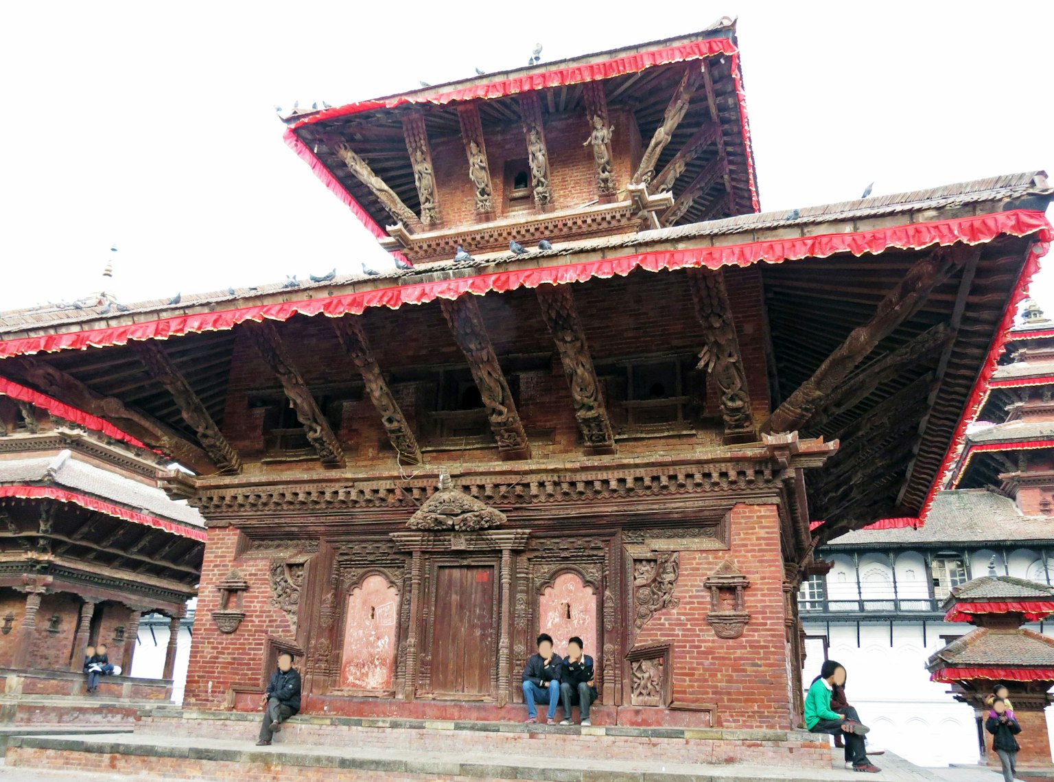 Vista exterior de un templo nepalés histórico con intrincadas tallas de madera y un techo rojo