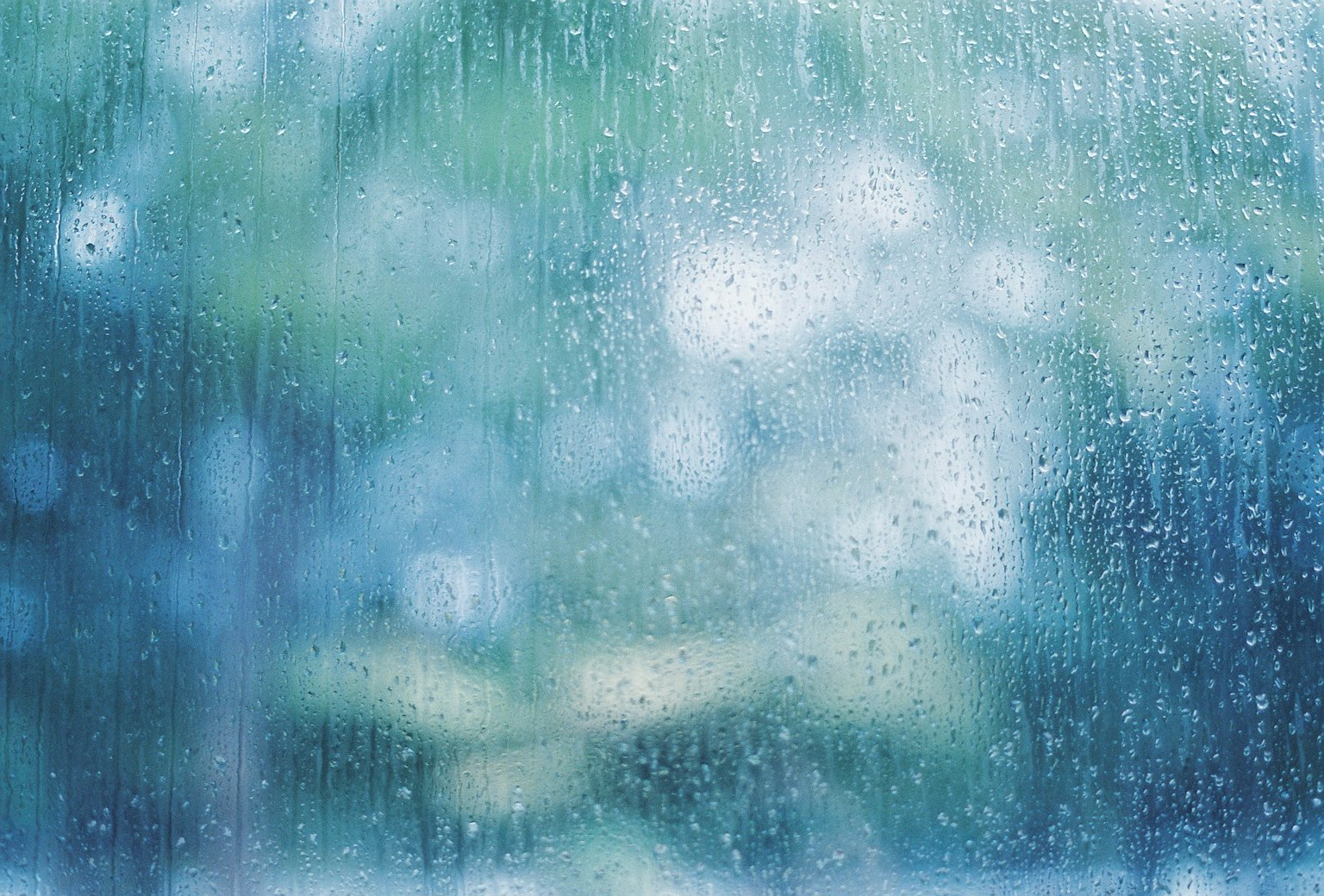 Raindrops flowing down a window with a blurred blue background