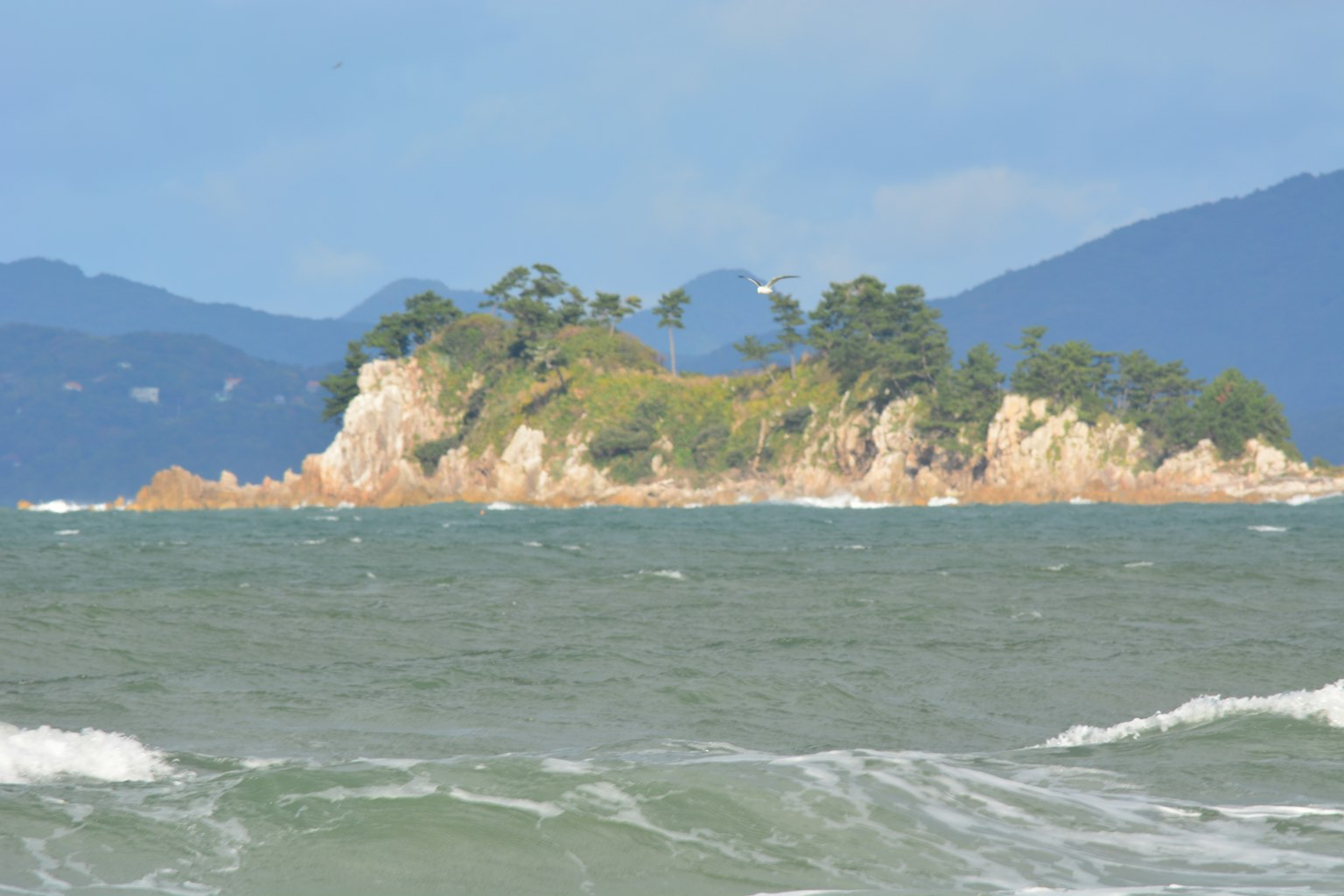 Pulau kecil dikelilingi air dengan gunung jauh