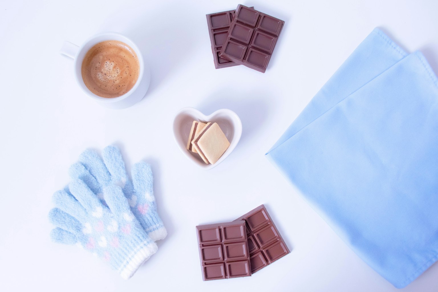 Szene mit Kaffee, Schokolade, Keksen und Handschuhen auf einem blauen Tuch
