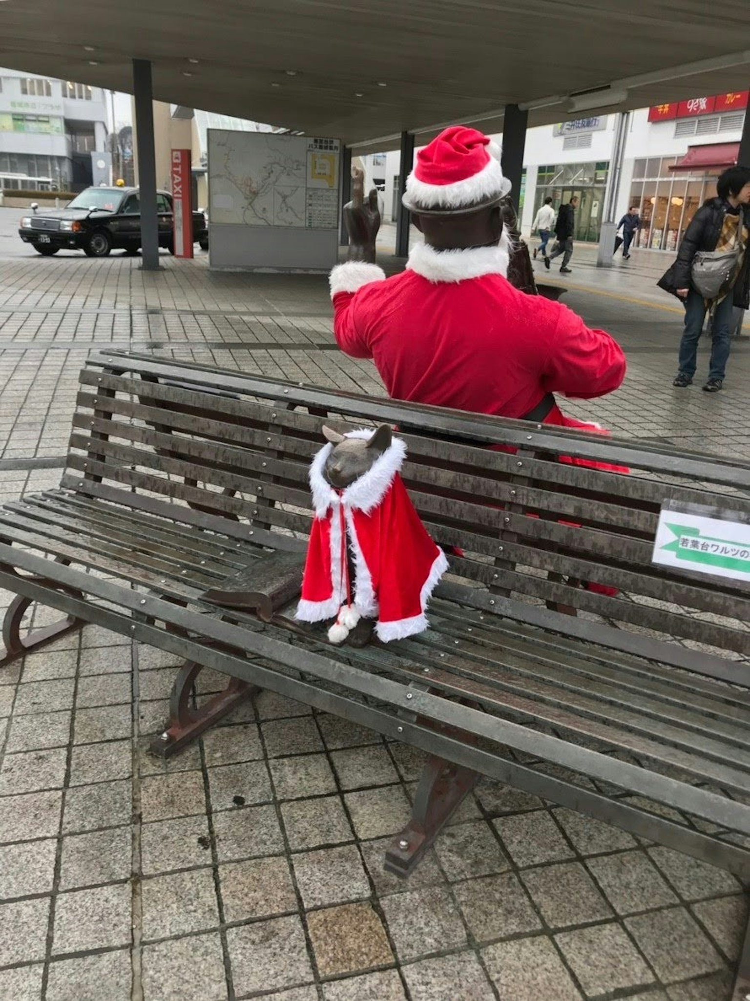 Personne en costume de Santa assise sur un banc avec un chien en manteau rouge à côté d'eux