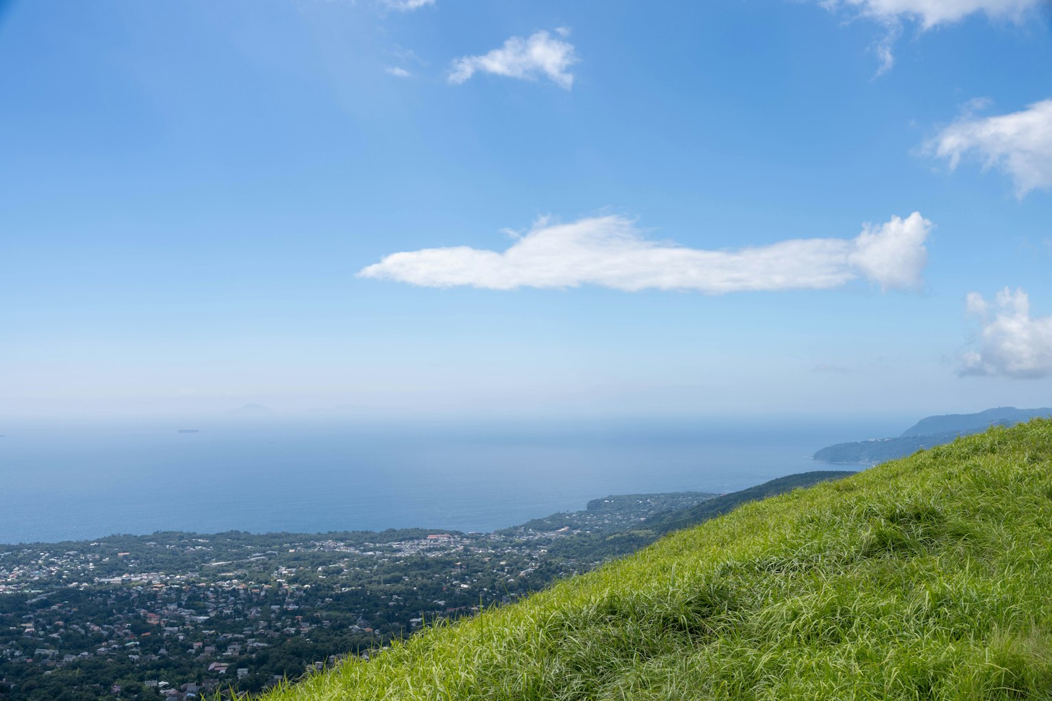 Grüne Hügel mit Blick auf ein ruhiges Meer und blauen Himmel mit Wolken