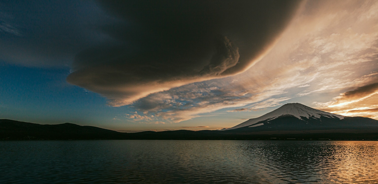 Scenic view of a mountain and lake with dramatic clouds at sunset