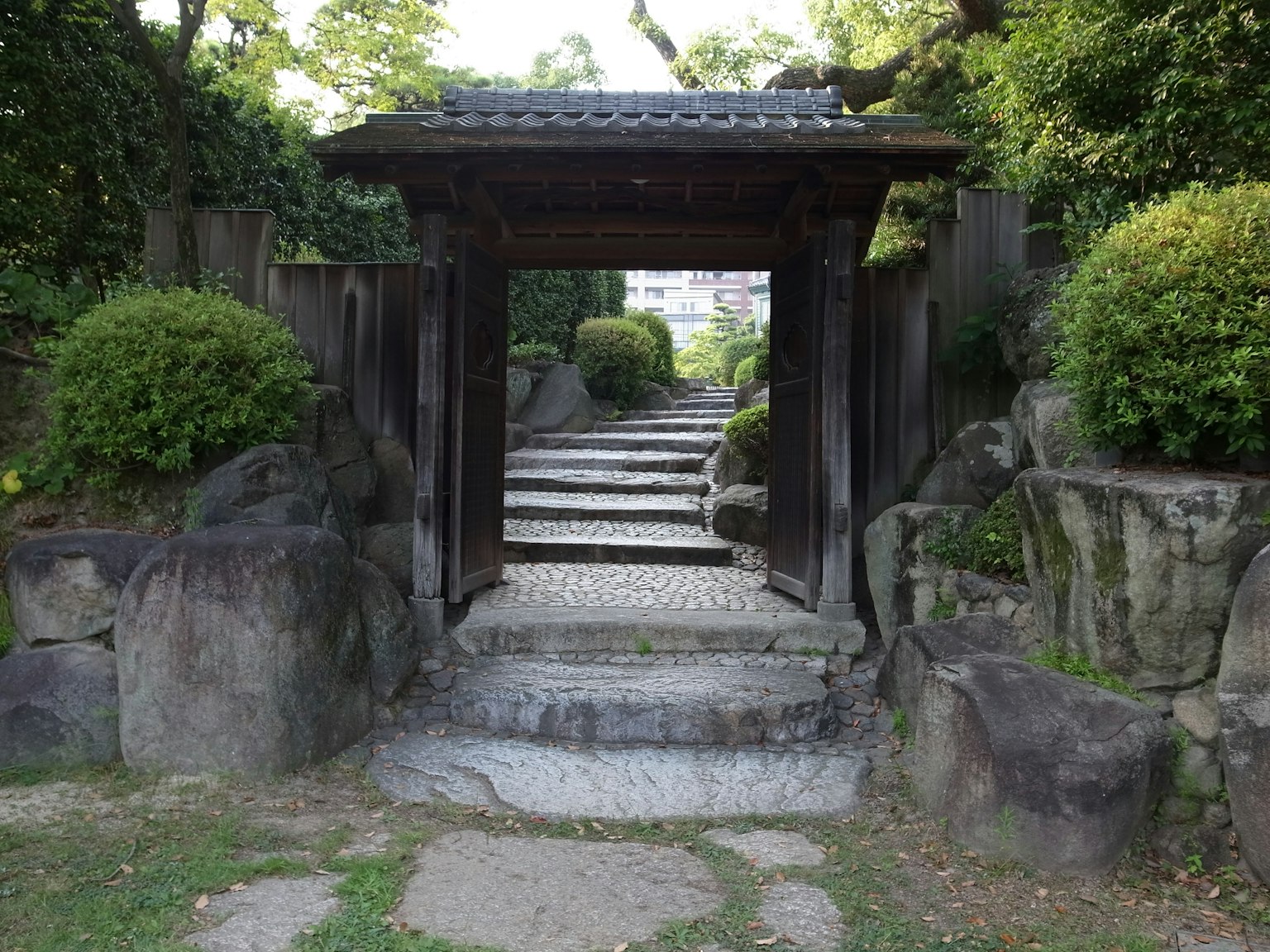 Entrada de un jardín japonés con una antigua puerta de madera y escalones de piedra