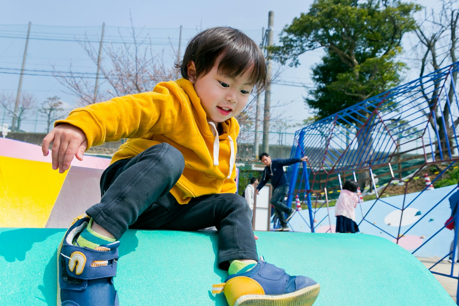 Seorang anak bermain di peralatan taman bermain mengenakan hoodie kuning