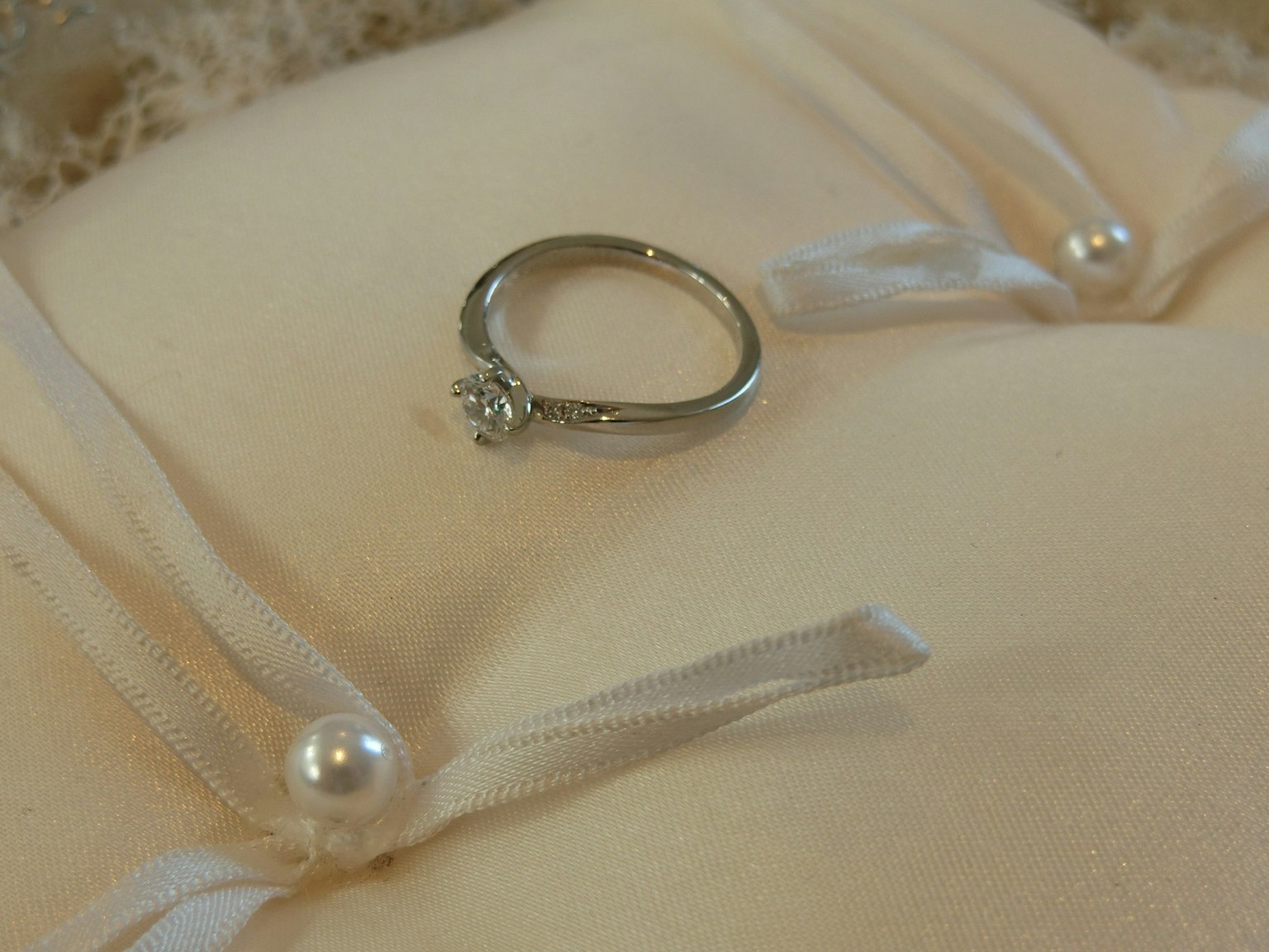 Anello di diamante su un cuscino color crema con dettagli in perla