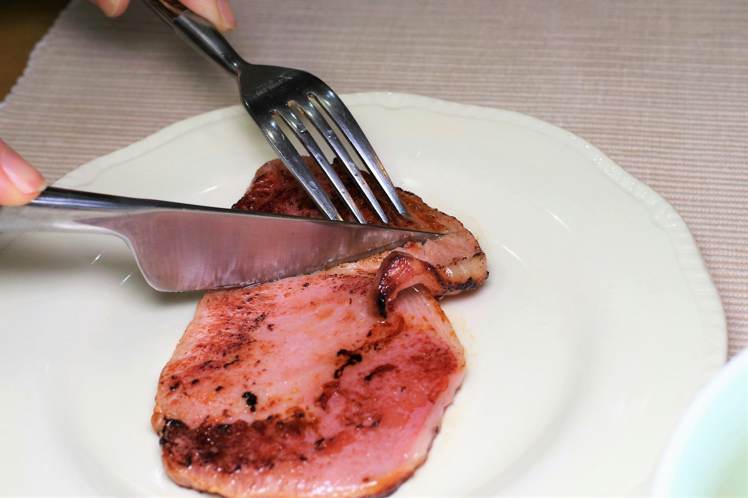 Eine Hand, die Fleisch auf einem Teller mit einem Messer und einer Gabel schneidet