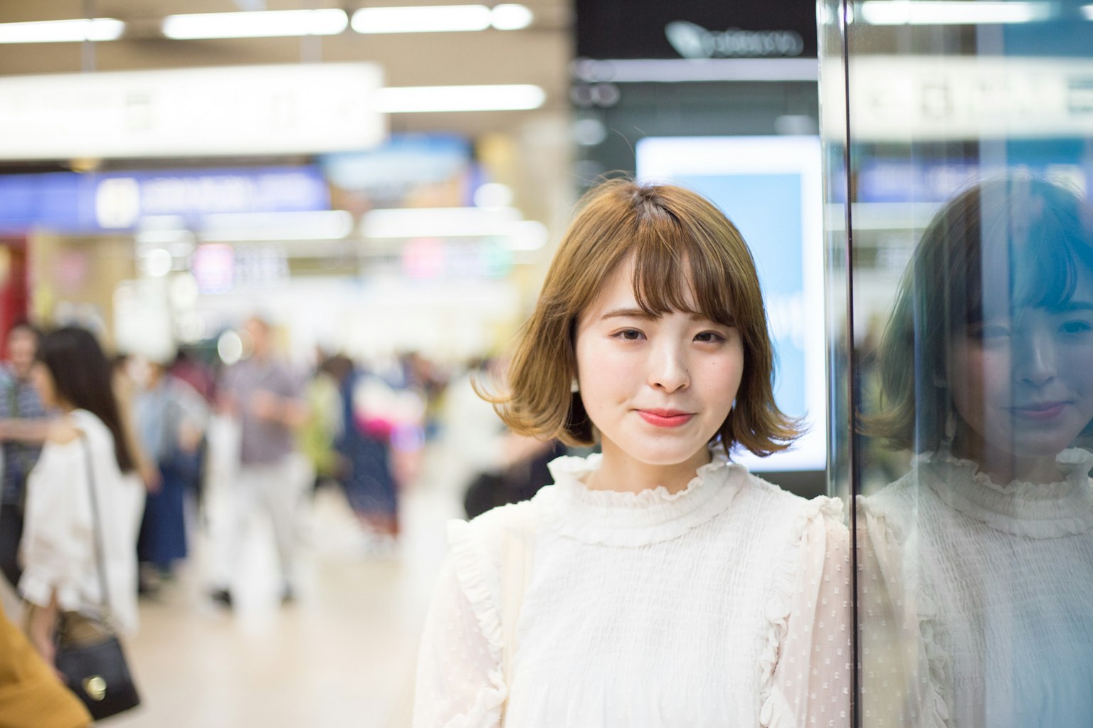 A smiling woman standing near a station with people walking in the background
