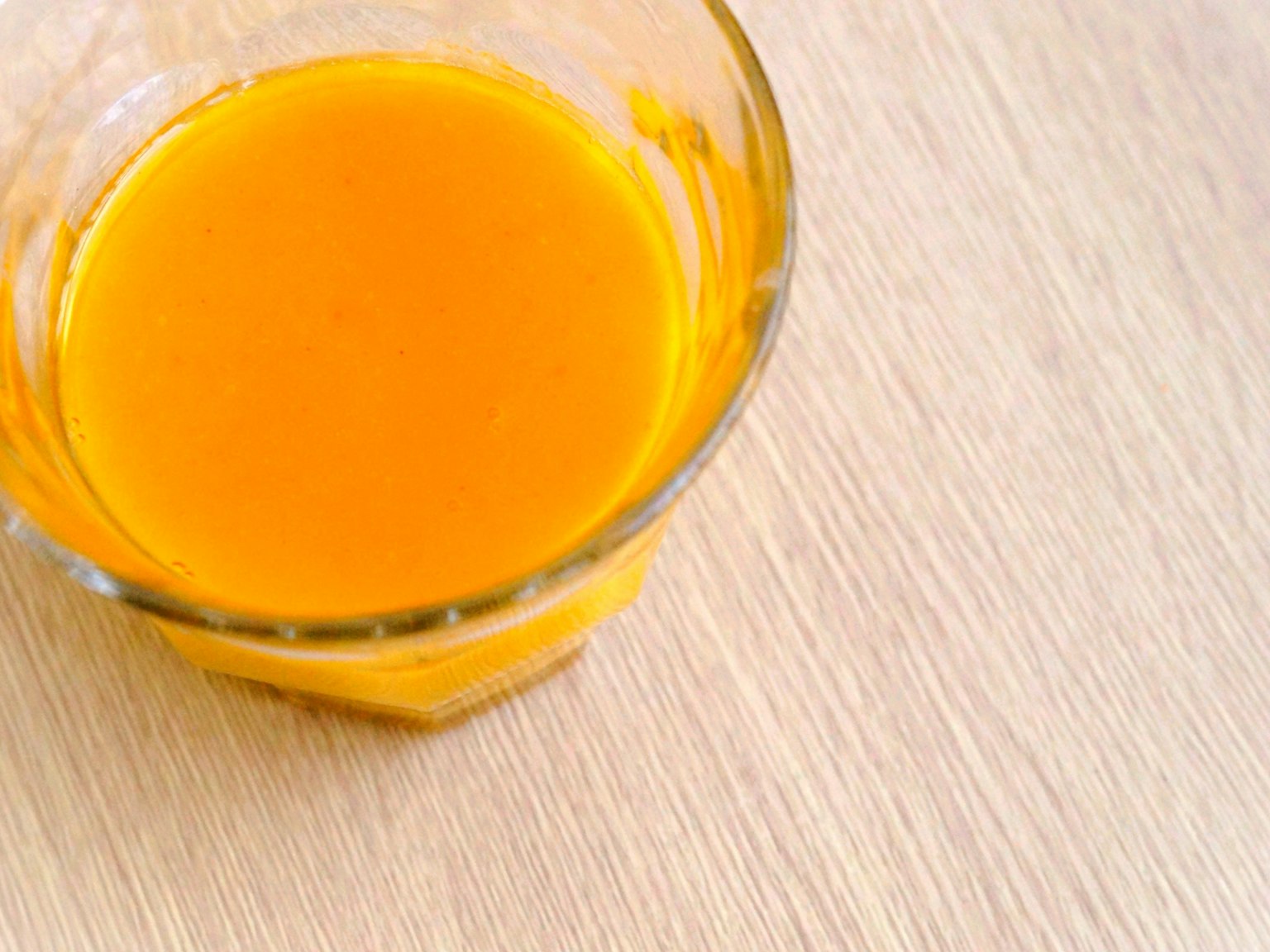 A glass bowl filled with orange juice placed on a wooden table