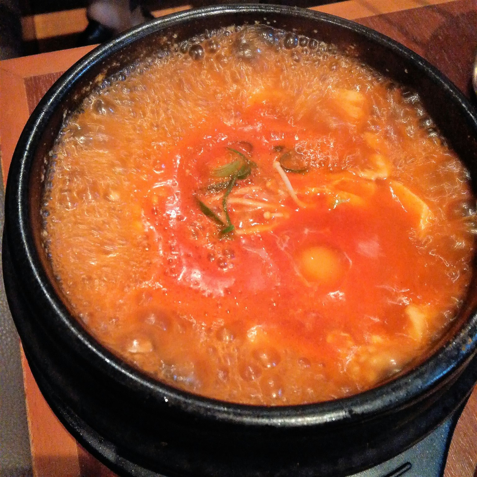 Nahaufnahme einer brodelnden Suppe in einem Steintopf mit einem Hauch von grünem Kraut