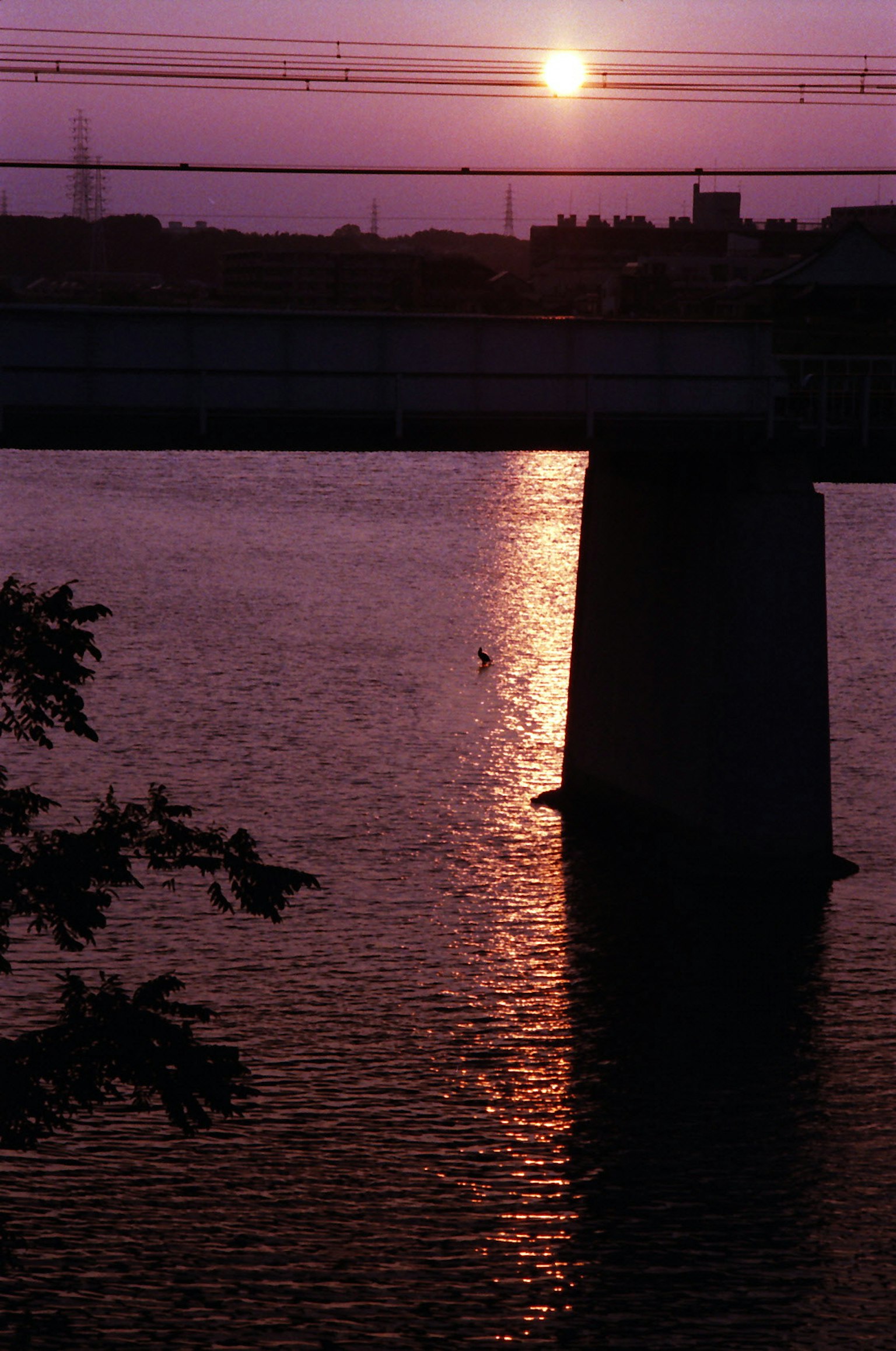 Silhouette einer Brücke gegen einen lila Sonnenuntergang mit Sonnenlicht, das sich im Wasser spiegelt