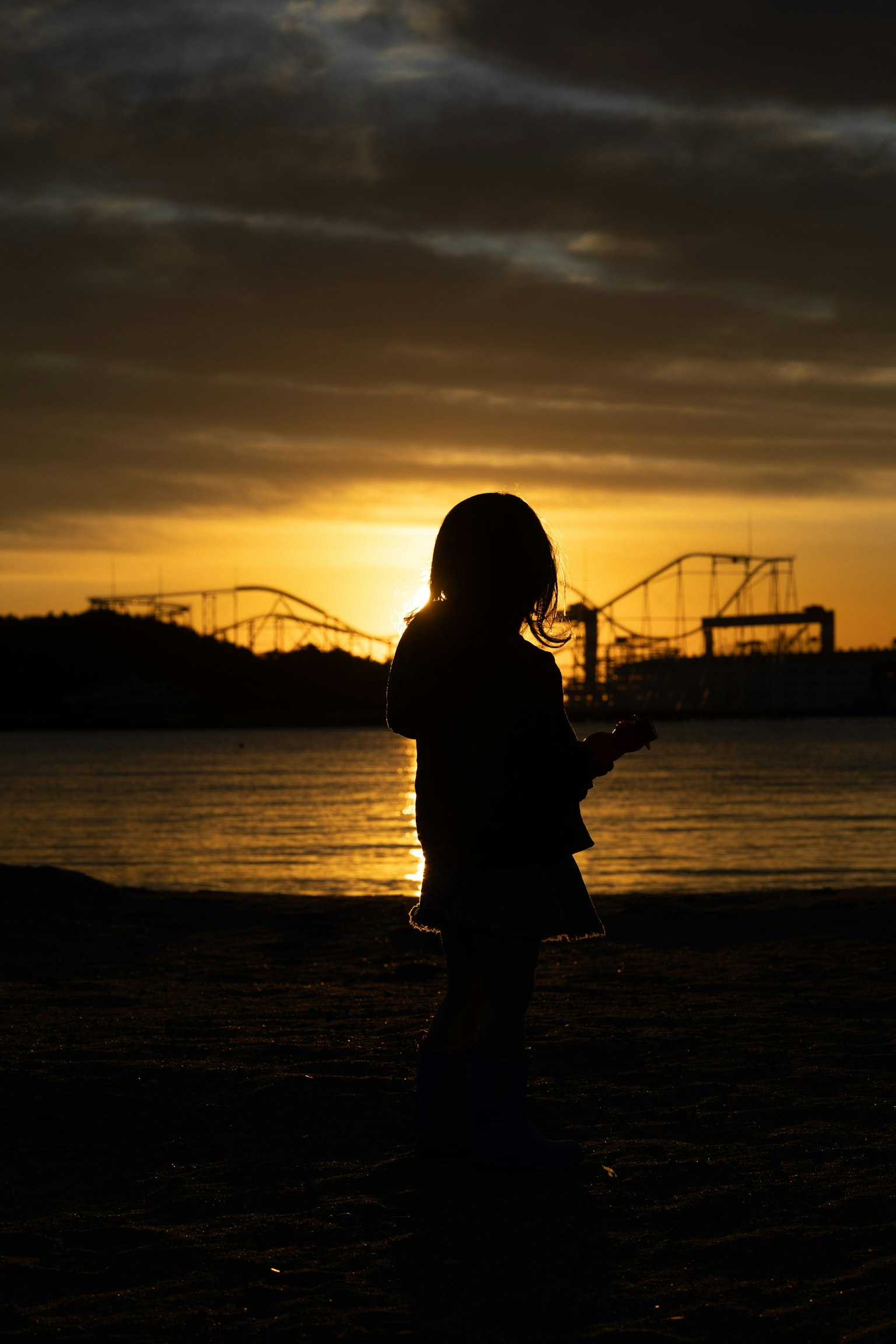 Silhouette d'un enfant au coucher de soleil avec des montagnes russes de parc d'attractions en arrière-plan