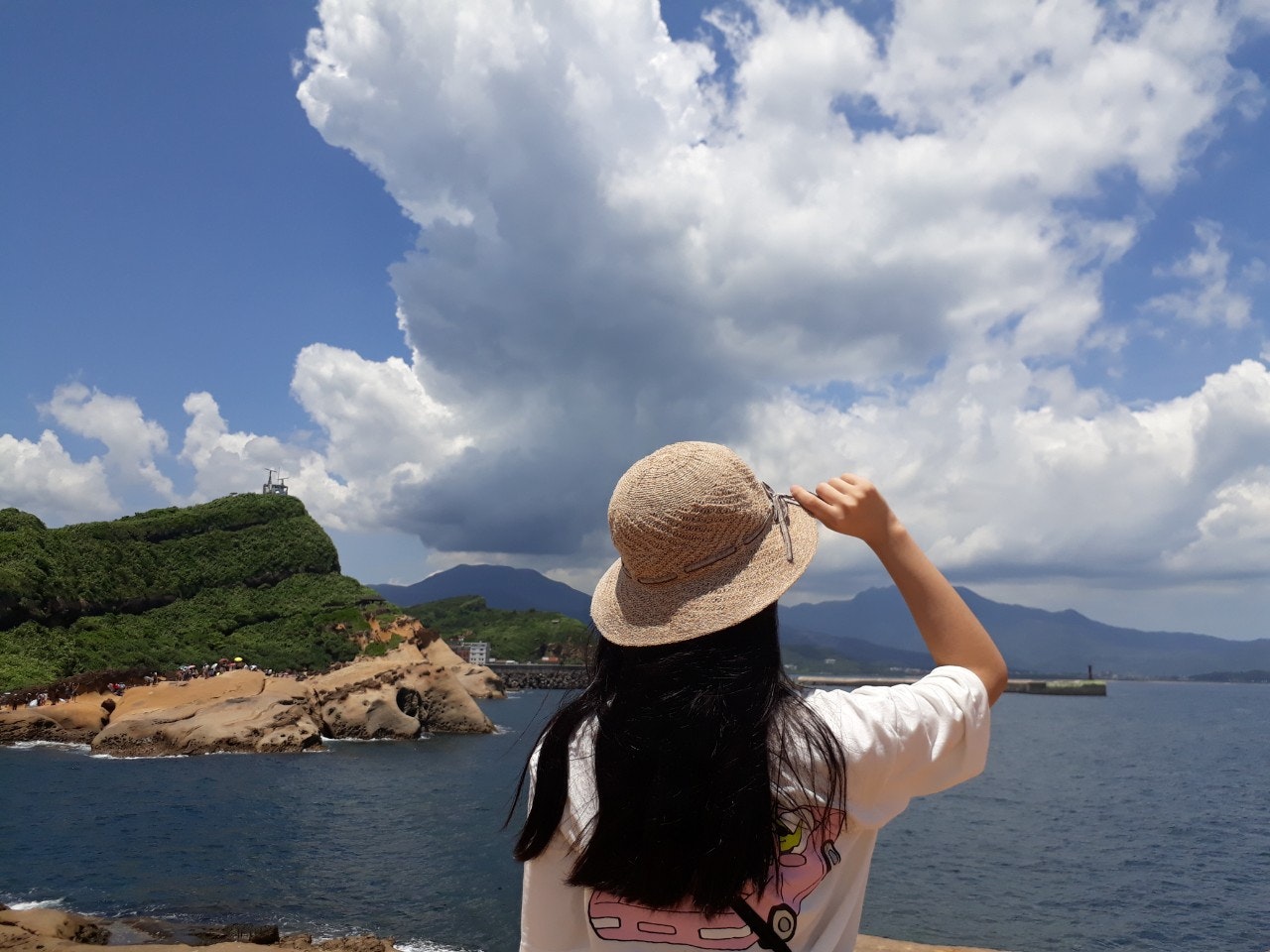 海辺で帽子をかぶる女性の後ろ姿