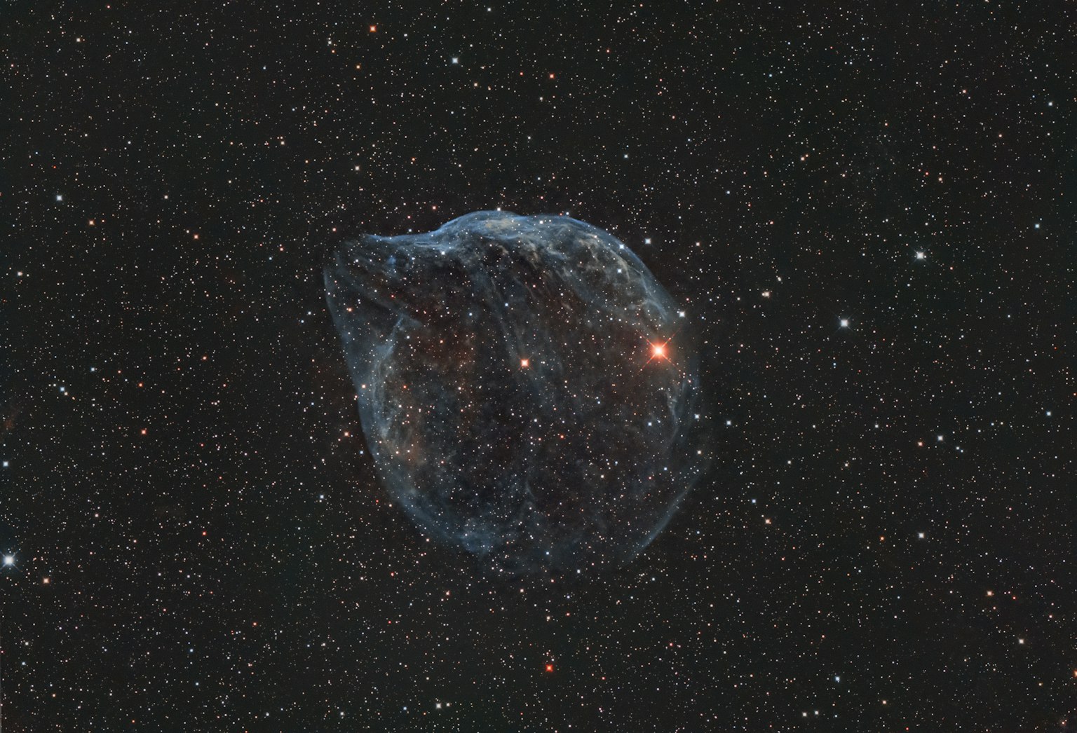 Image détaillée d'une nébuleuse dans l'espace avec un arrière-plan bleu et noir et des étoiles brillantes ainsi qu'un point lumineux orange à l'intérieur de la nébuleuse