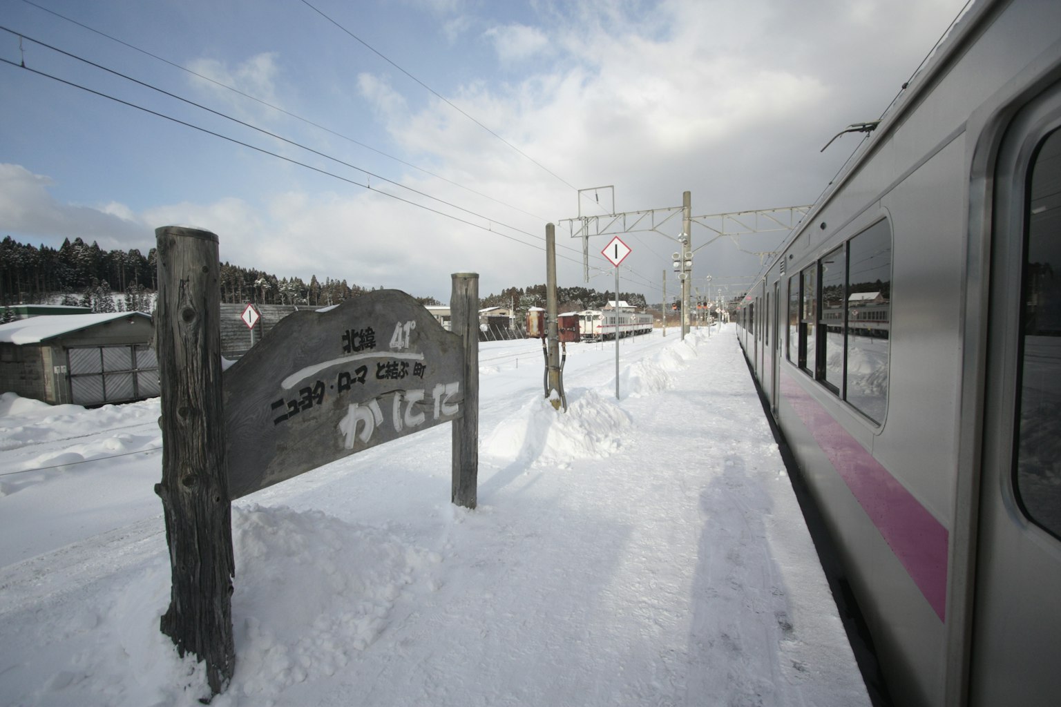 Ein schneebedeckter Bahnhof mit einem Zug und einem Holzschild