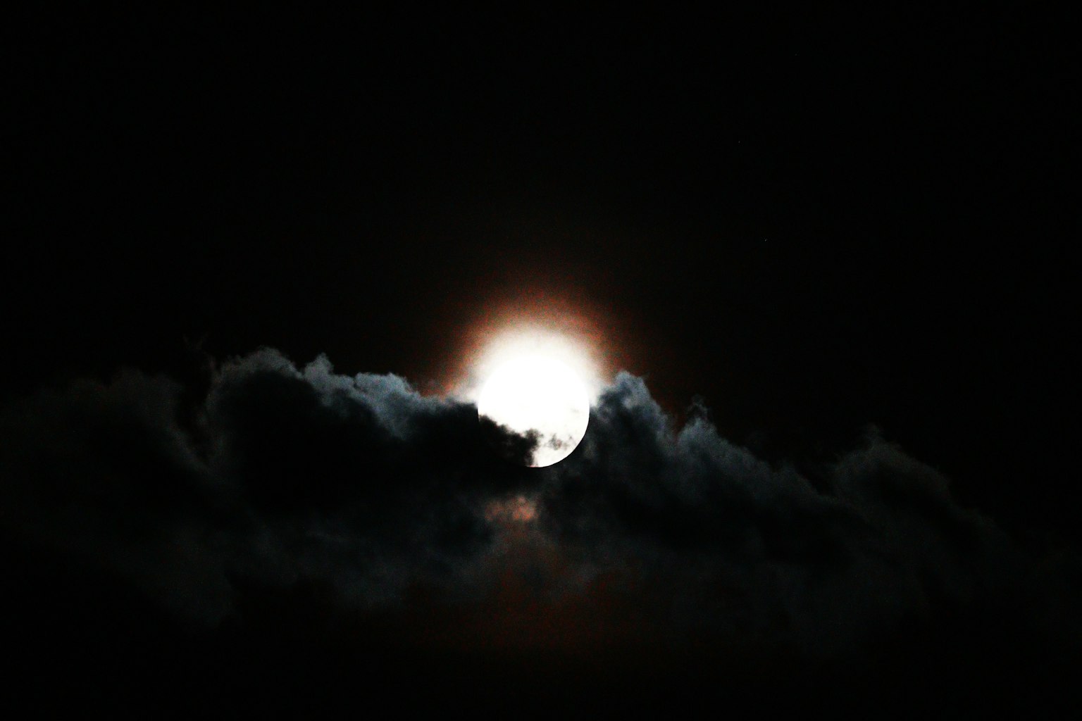 Helle Mond umgeben von dunklen Wolken in einem schwarzen Himmel
