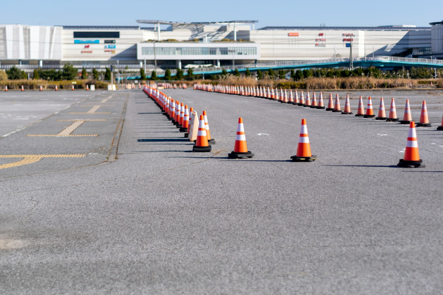 Cônes orange et blanc alignés dans un parking avec un bâtiment en arrière-plan