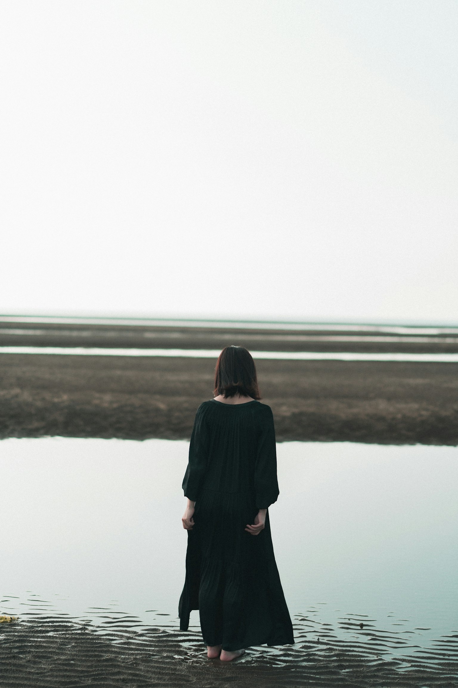 Una mujer con un vestido negro de pie junto al agua