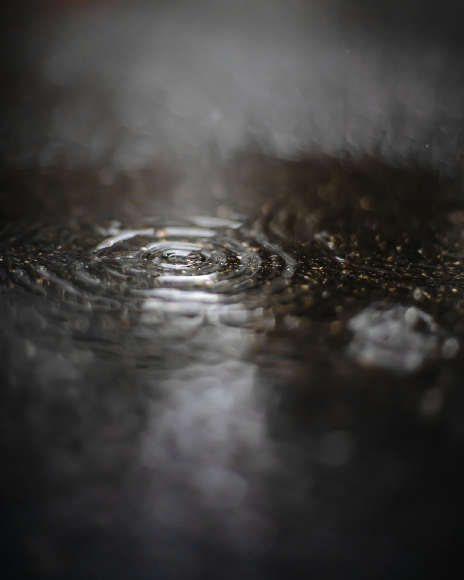 在黑暗表面上的水窪中雨滴產生的漣漪圖像