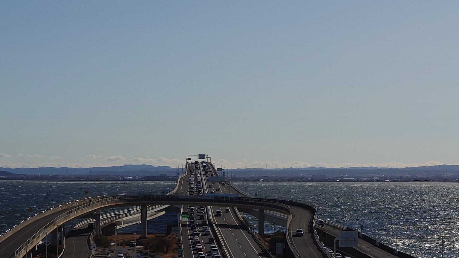 Un puente rodeado de cielo y mar azules con flujo de tráfico visible