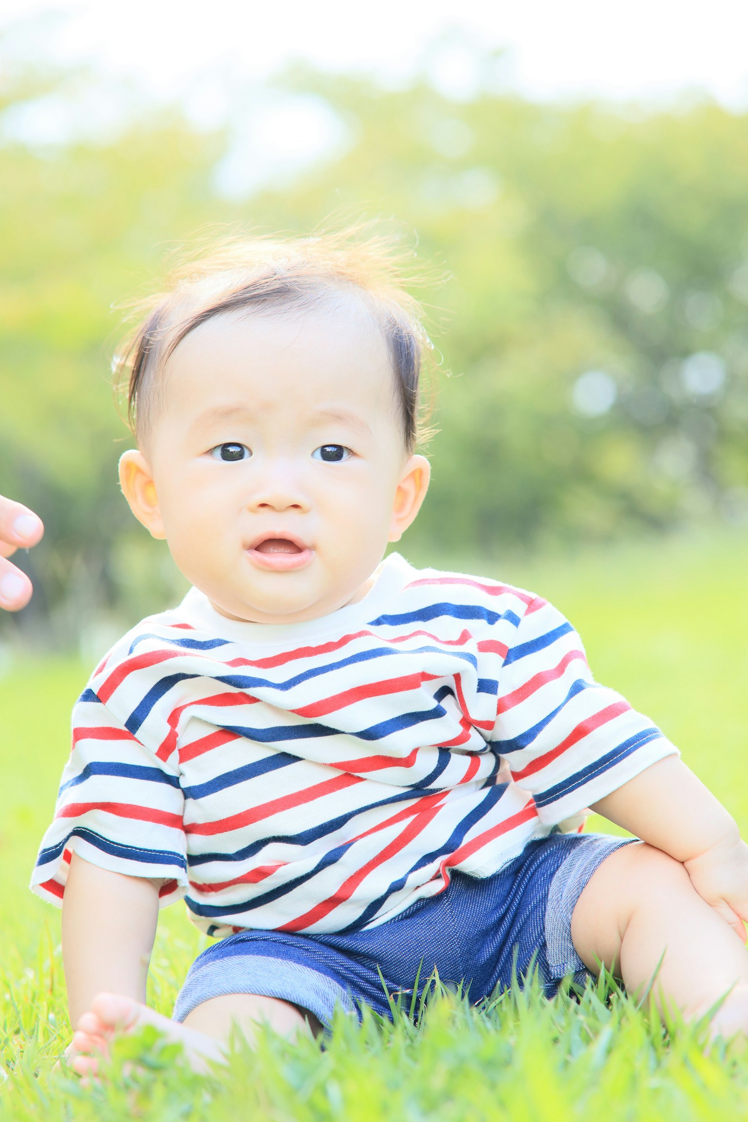 풀밭에 앉아 있는 아기의 사진으로 줄무늬 셔츠를 입고 있다