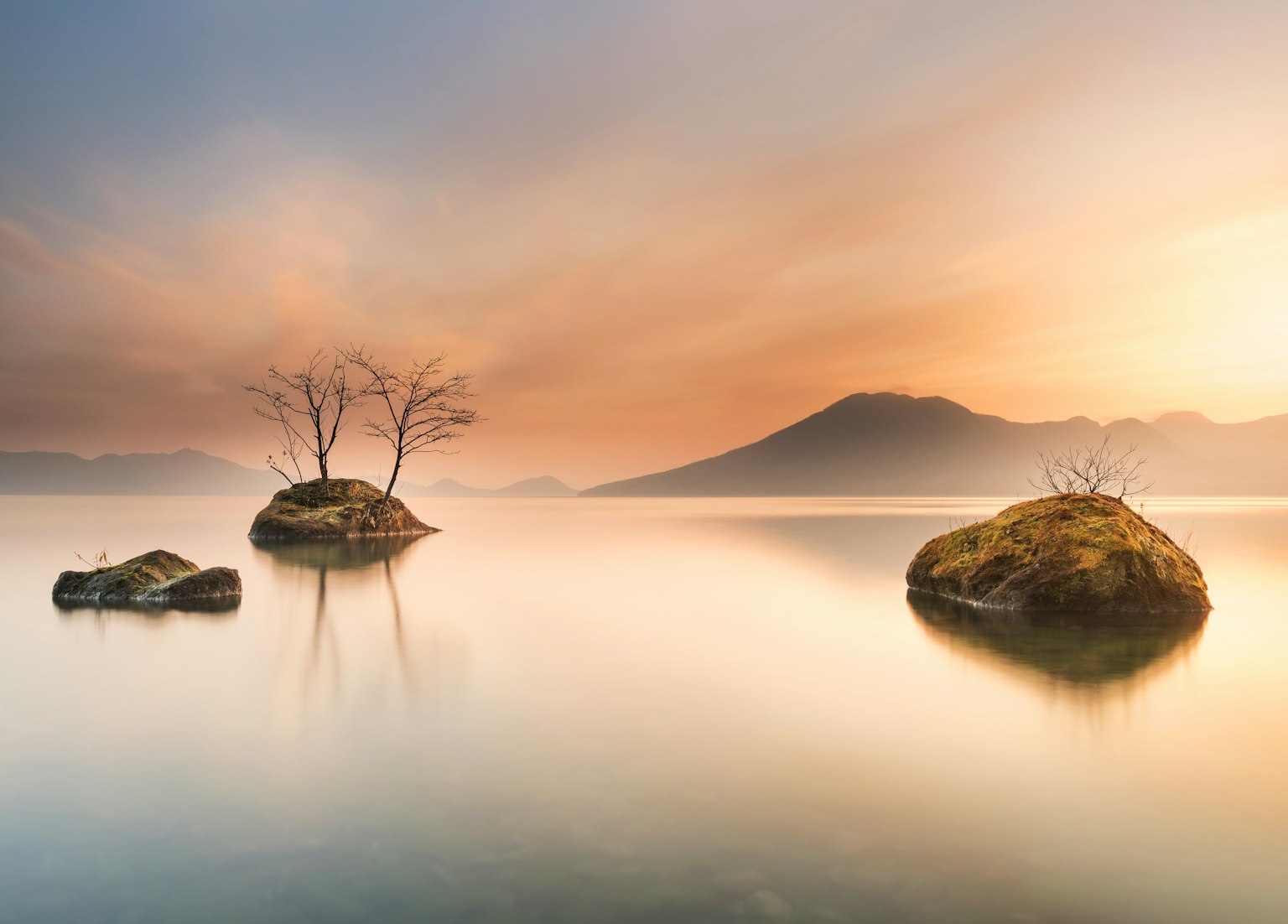 Serene lake landscape with small islands and mountain silhouette