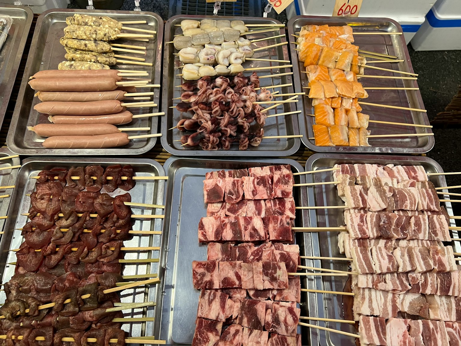 Imagen de brochetas exhibidas en un puesto de comida varios ingredientes en brochetas dispuestos en bandejas