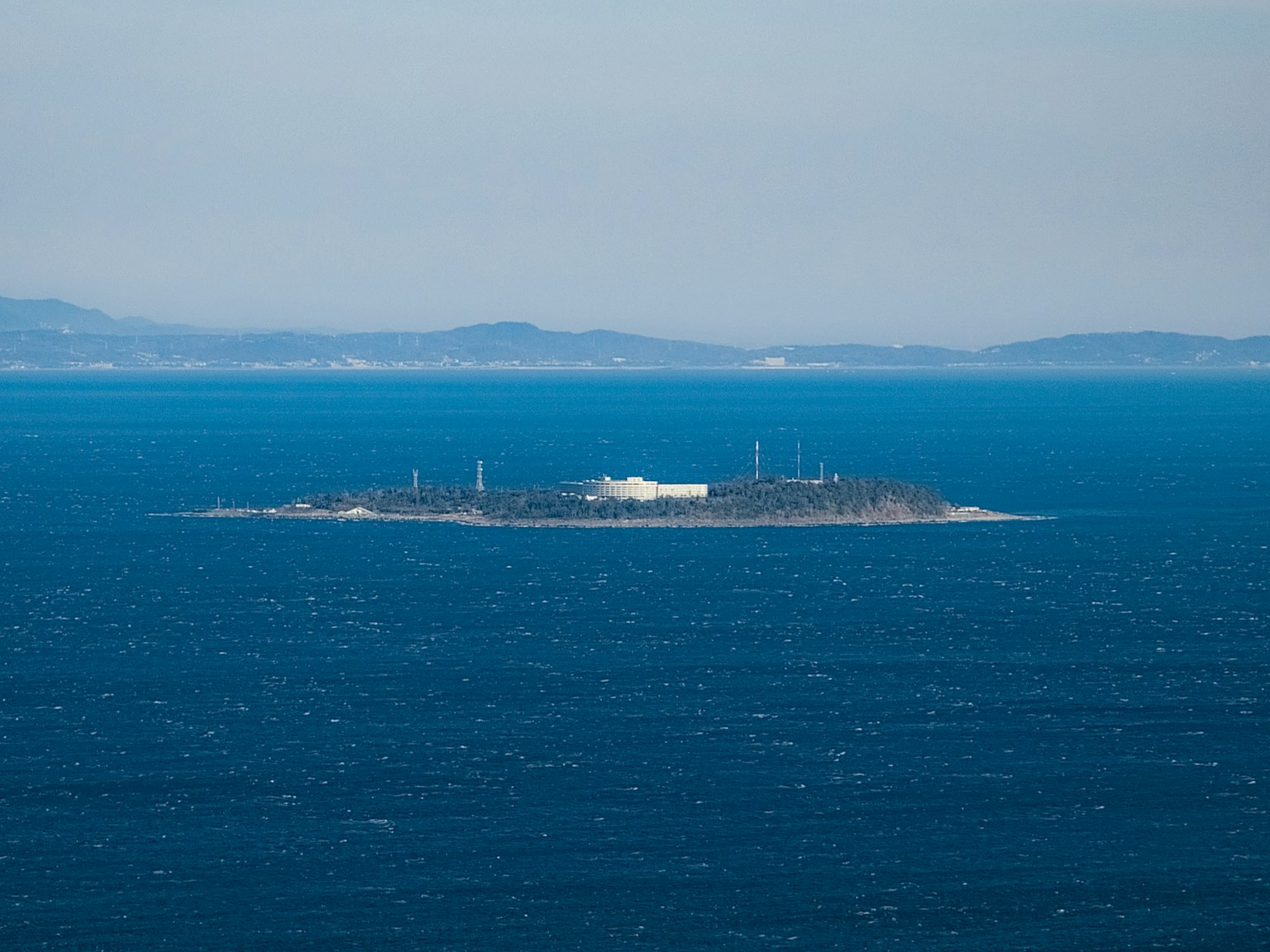 青い海に浮かぶ小さな島とその上の白い建物