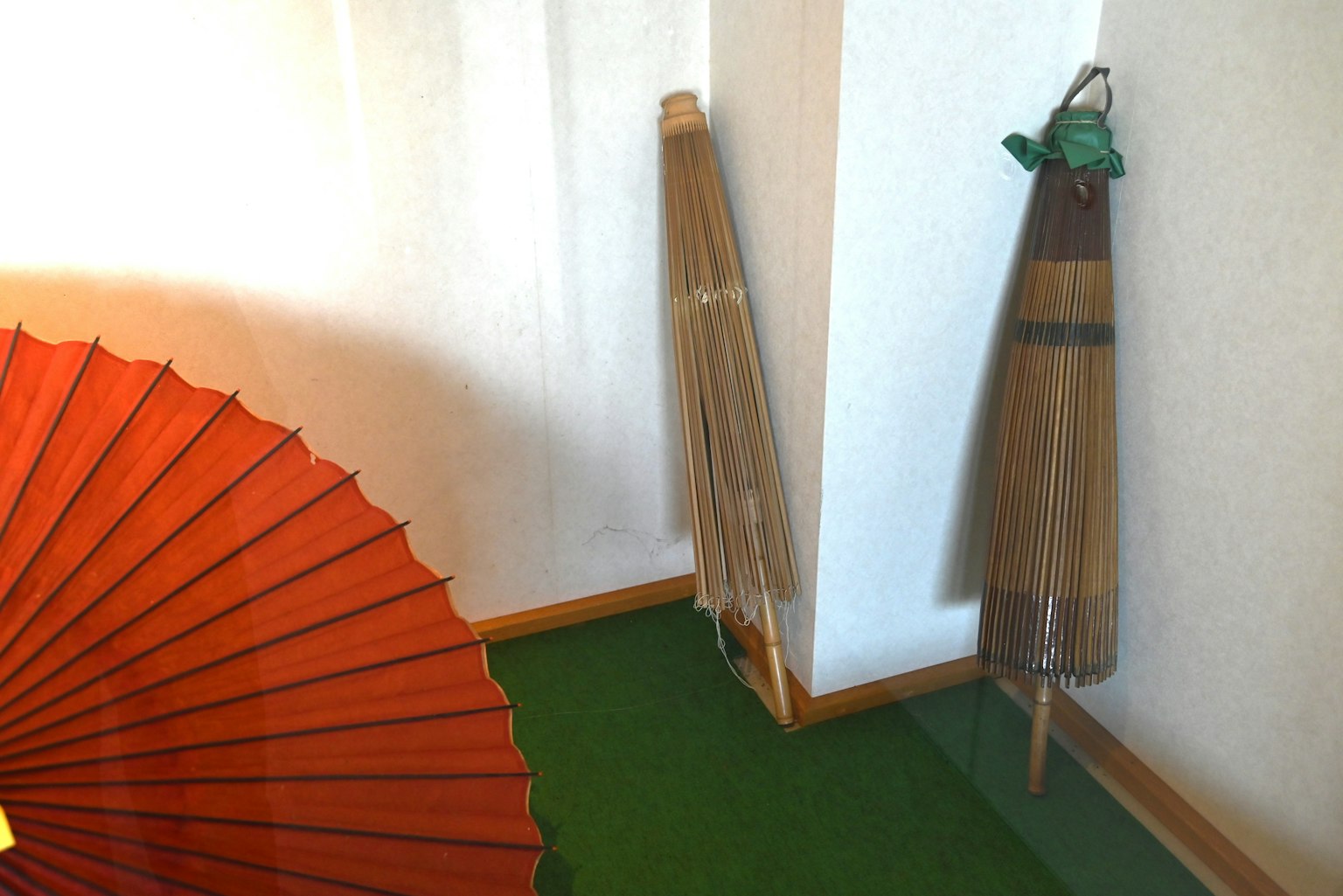 Escena interior con un paraguas tradicional rojo y paraguas de bambú apoyados en la pared