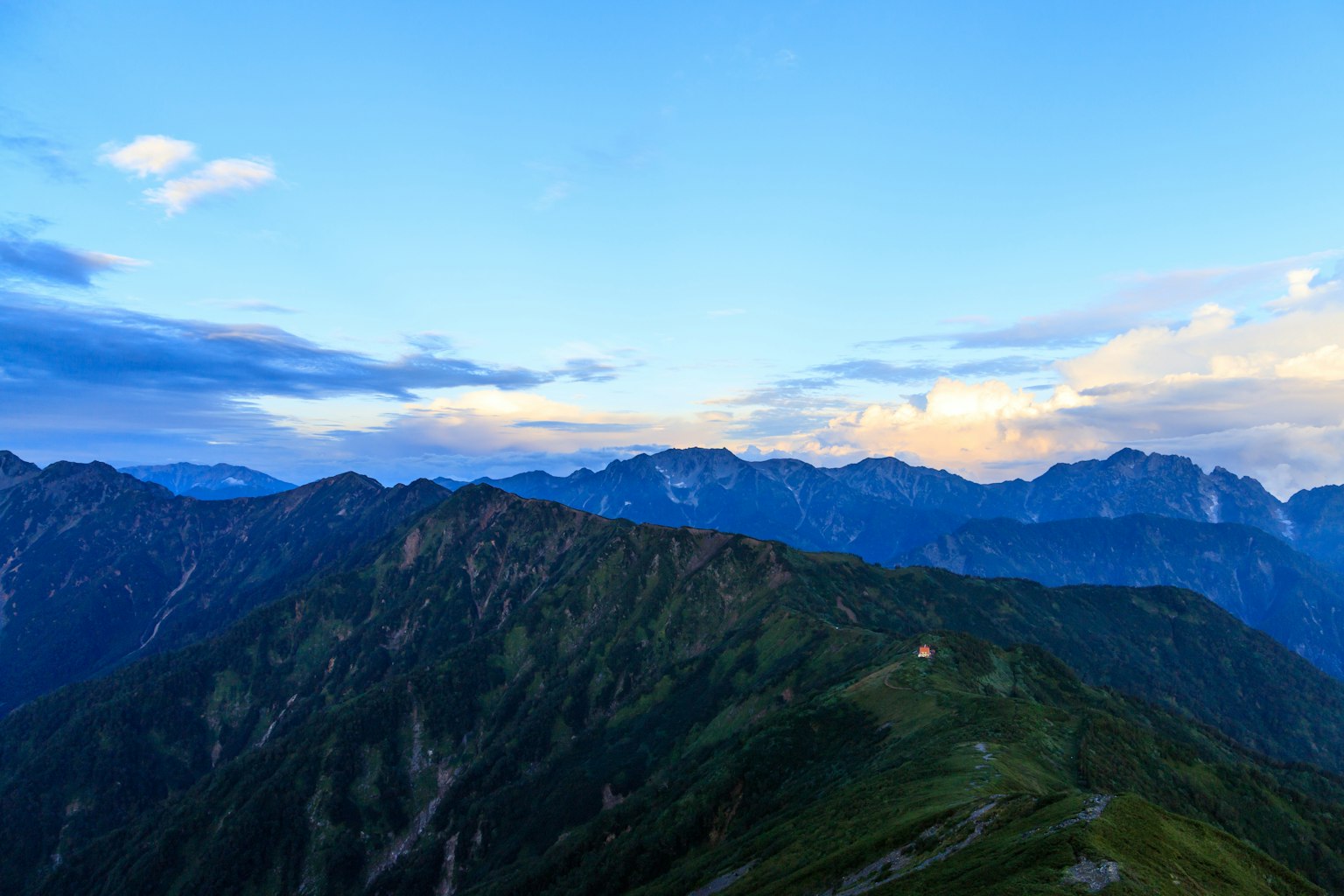 Pemandangan gunung di bawah langit biru dengan awan Bukit hijau dan puncak jauh terlihat