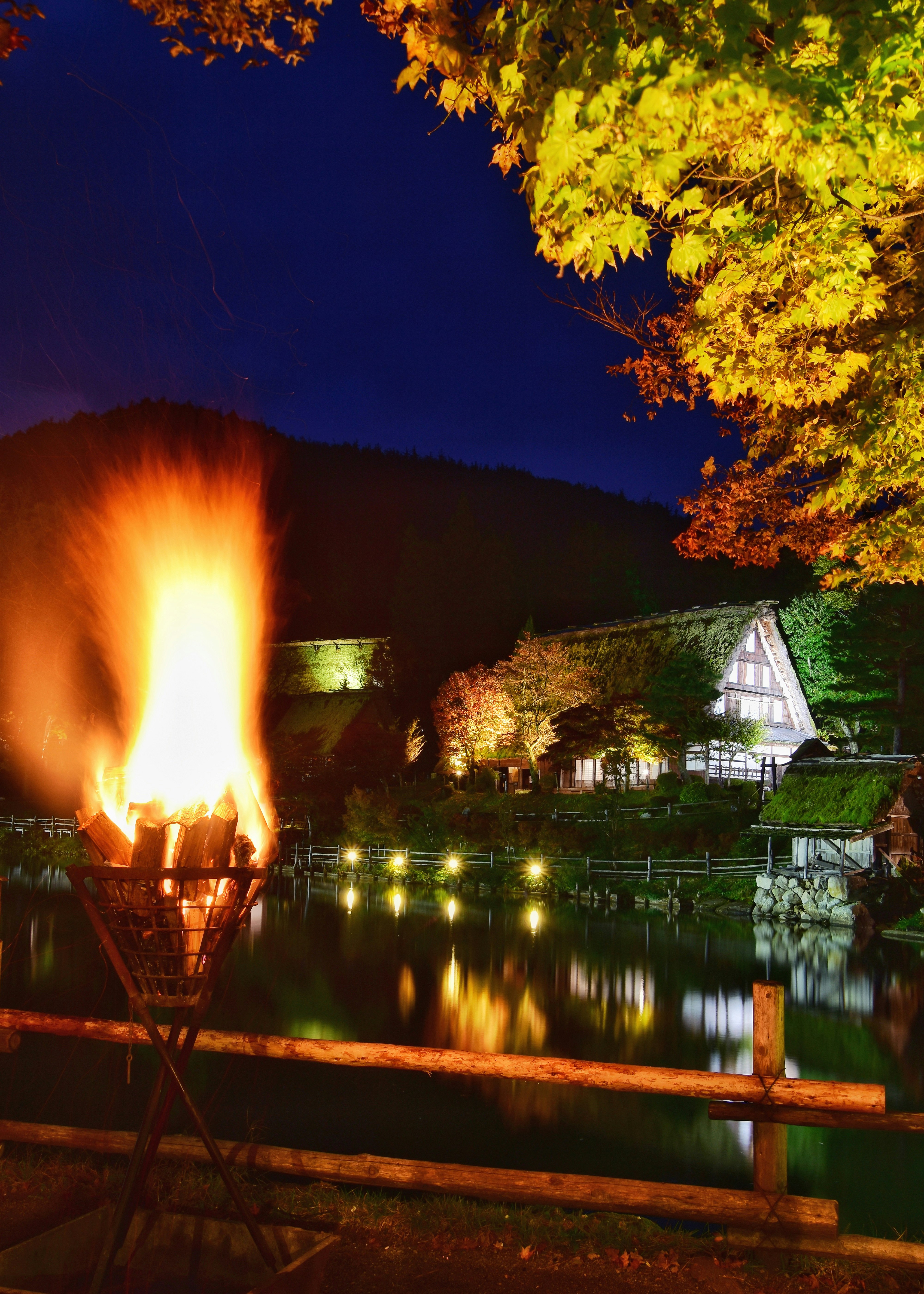 飛騨民俗村の池と茅葺き家屋、秋の紅葉が映る夜景