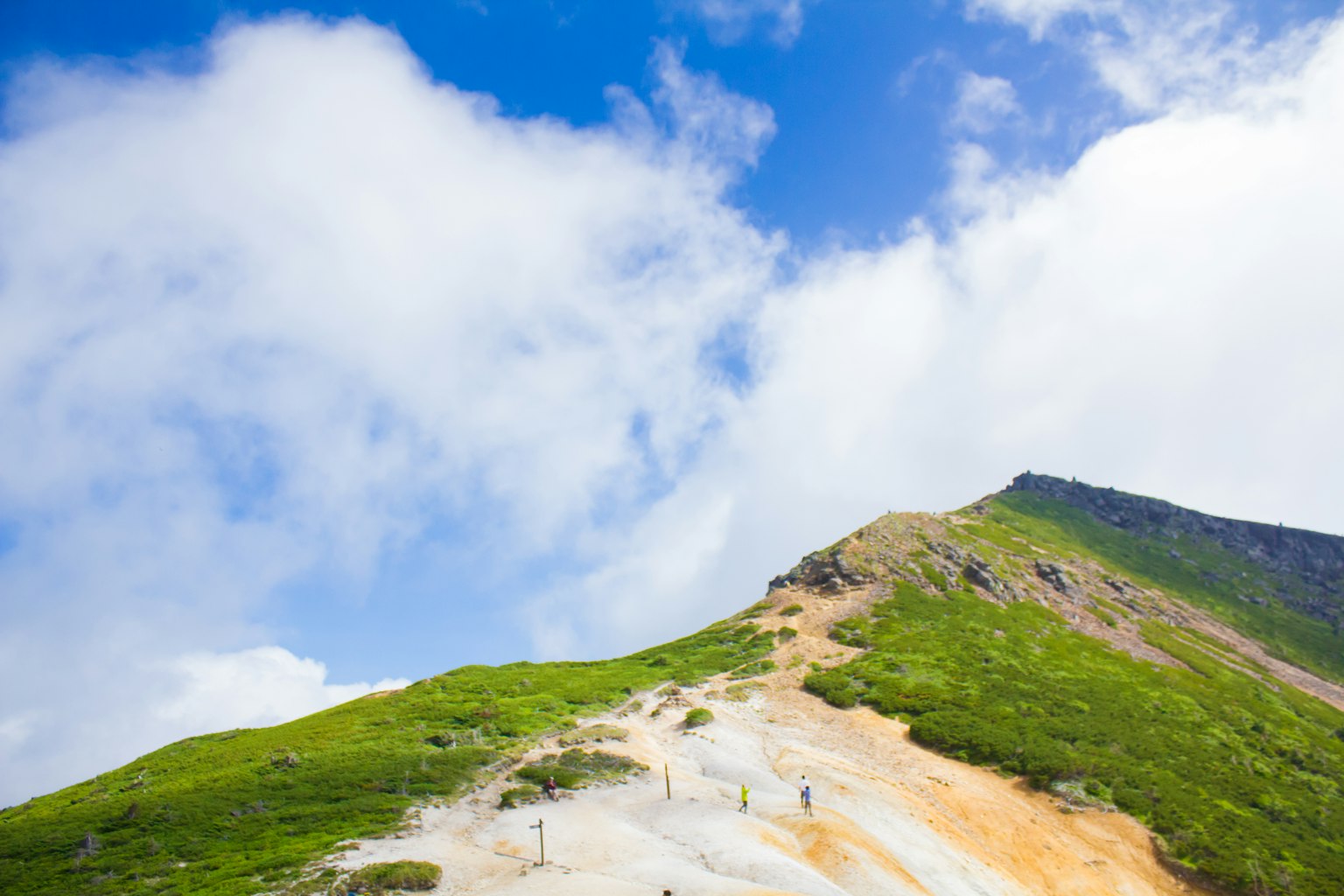 Mountain landscape with green slopes and blue sky featuring hikers