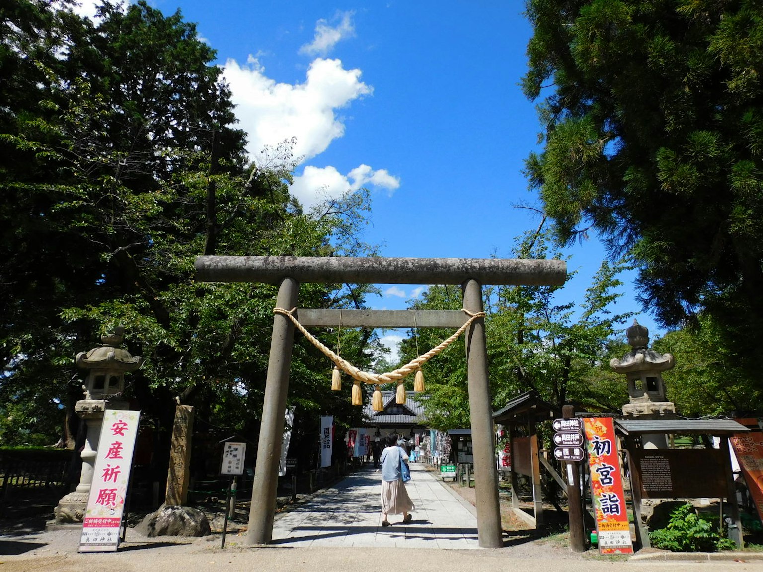 Seseorang yang berjalan melewati gerbang torii di kuil di bawah langit biru